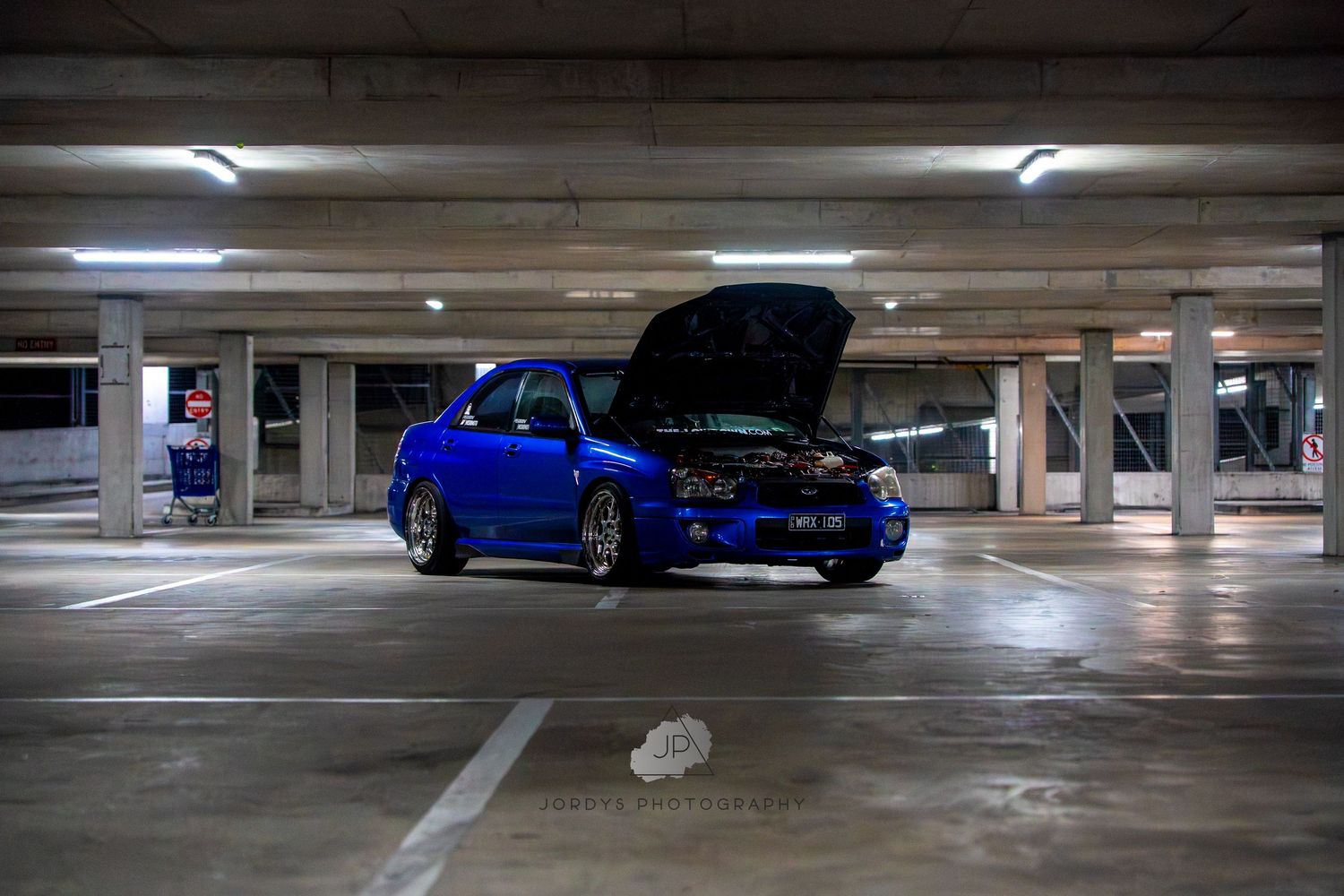 Low-light view of empty concrete parking garage with fluorescent lighting overhead showing multiple levels and parking spots.