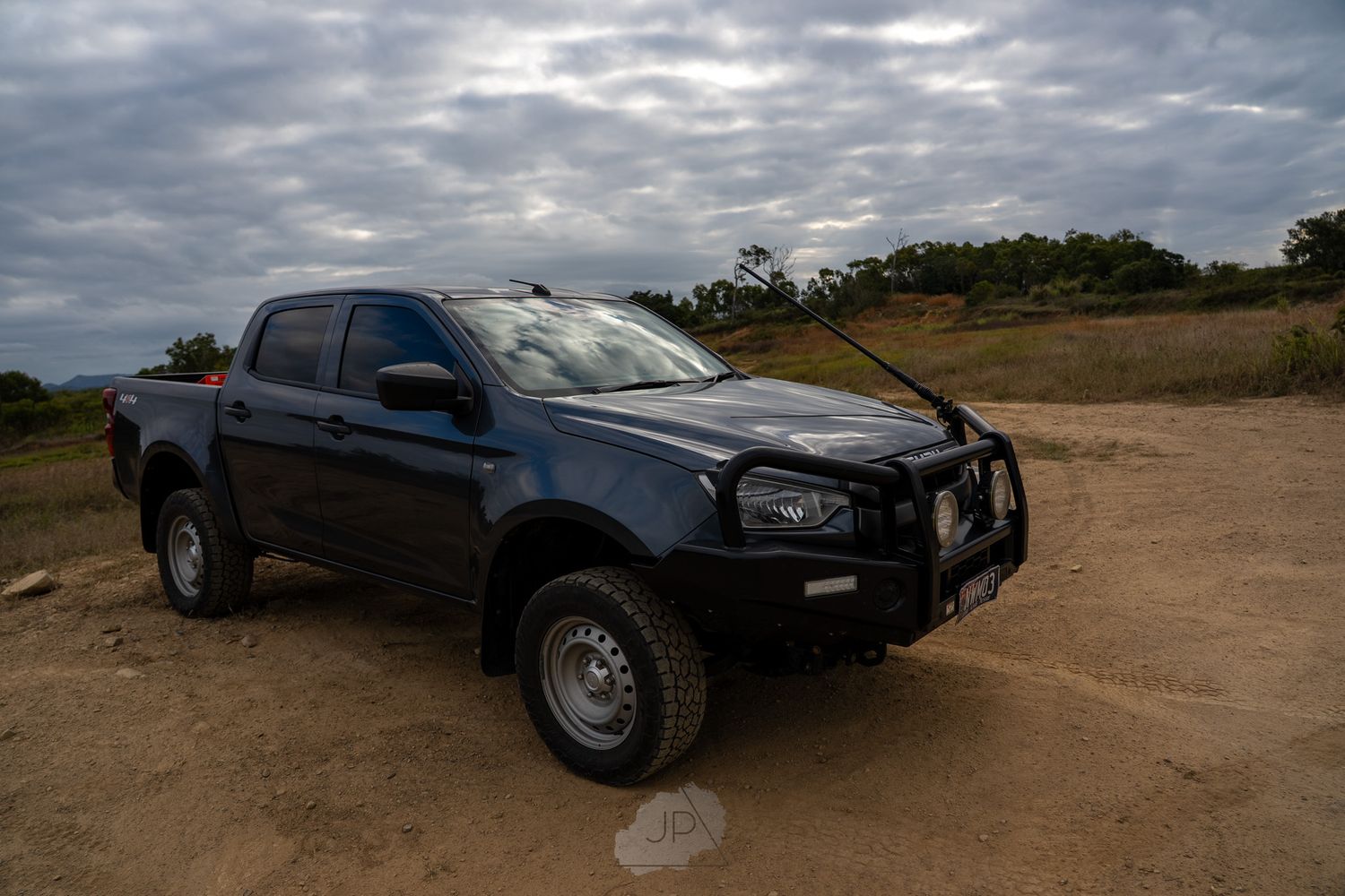 Black pickup truck driving across a rugged desert terrain under cloudy skies.