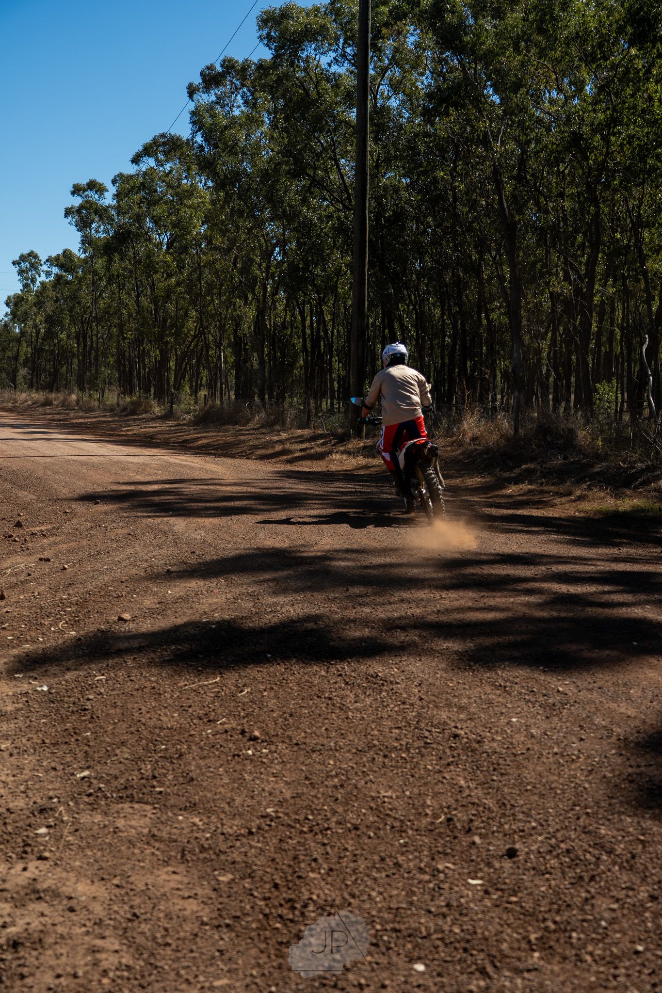A dirt bike rider kicks up dust while riding through a eucalyptus forest on a winding dirt trail in Australia.