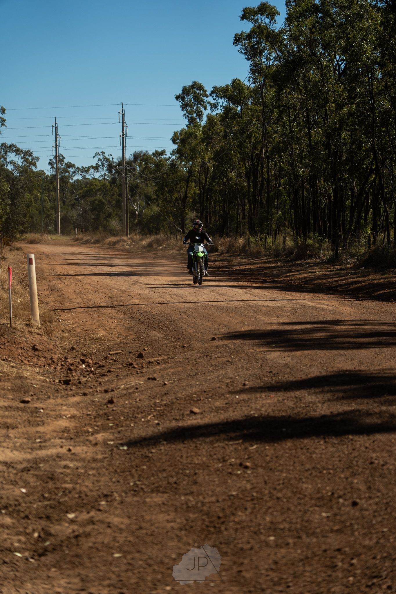 A dirt path winds through sparse bushland with power lines and trees visible in the rural Australian landscape.