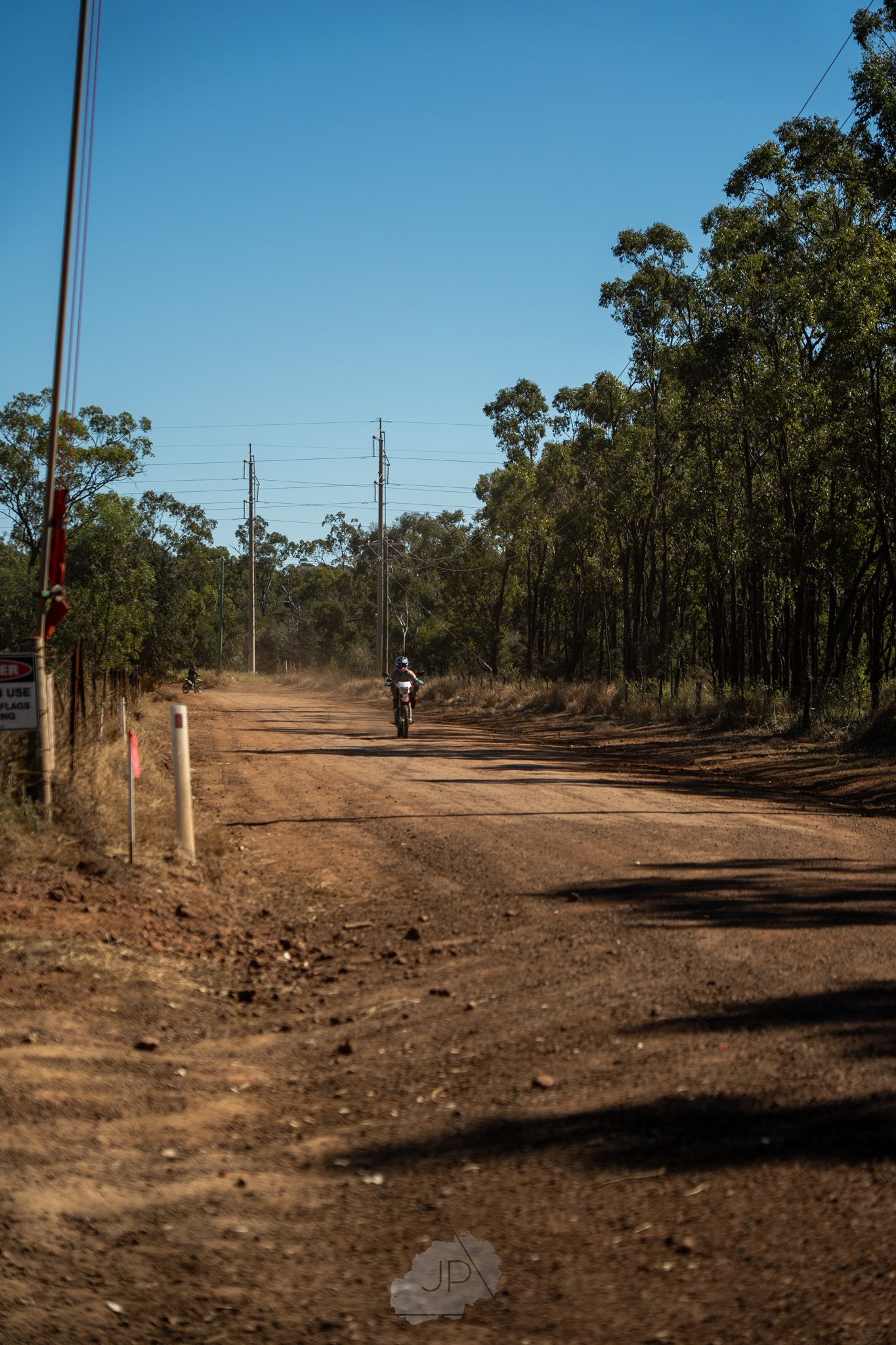 Dirt motocross track with winding path through wooded area on sunny day shows red trail markers along course.
