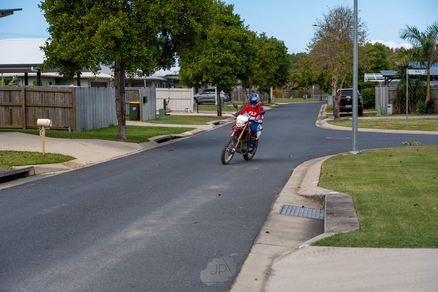 Scenic neighborhood street lined with green lawns and mature trees on a sunny day with a red motorcycle in view.