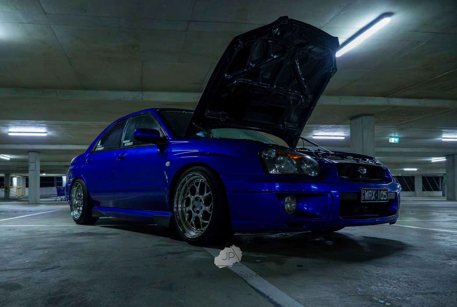Blue coupe car parked in a dimly lit indoor parking garage shown from multiple angles with hood open.