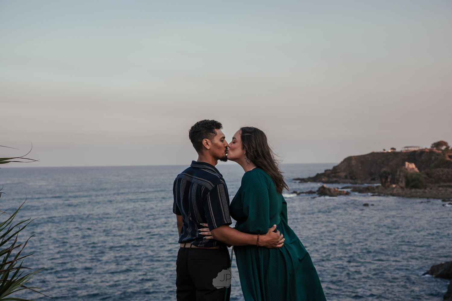 Silhouettes share an intimate moment on a dramatic coastal cliff against a twilight seascape.