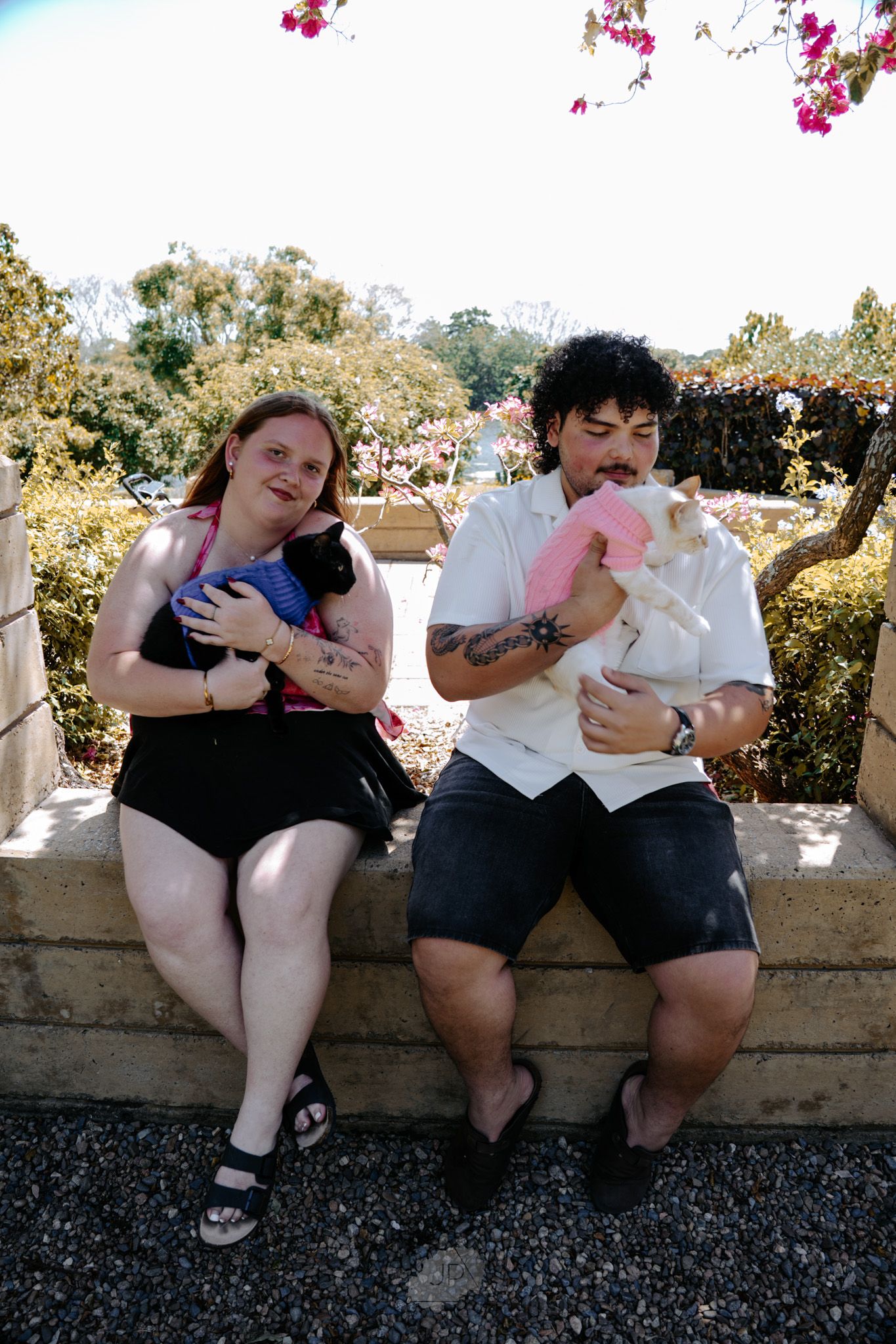 Two people sitting together on a stone wall sharing ice cream cones on a sunny day.