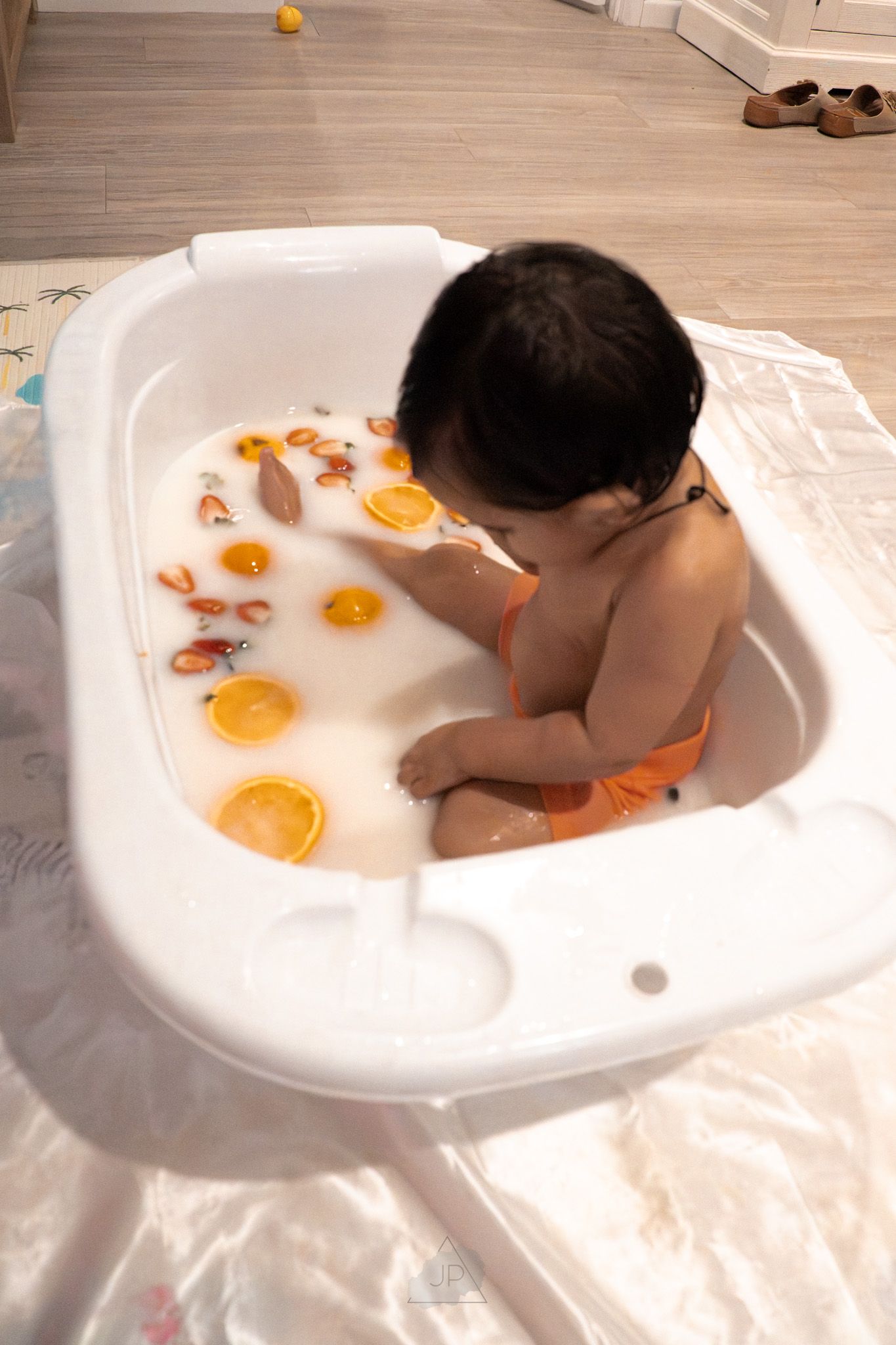 A series of images showing someone playing with oranges in a bathtub filled with white bubbles.