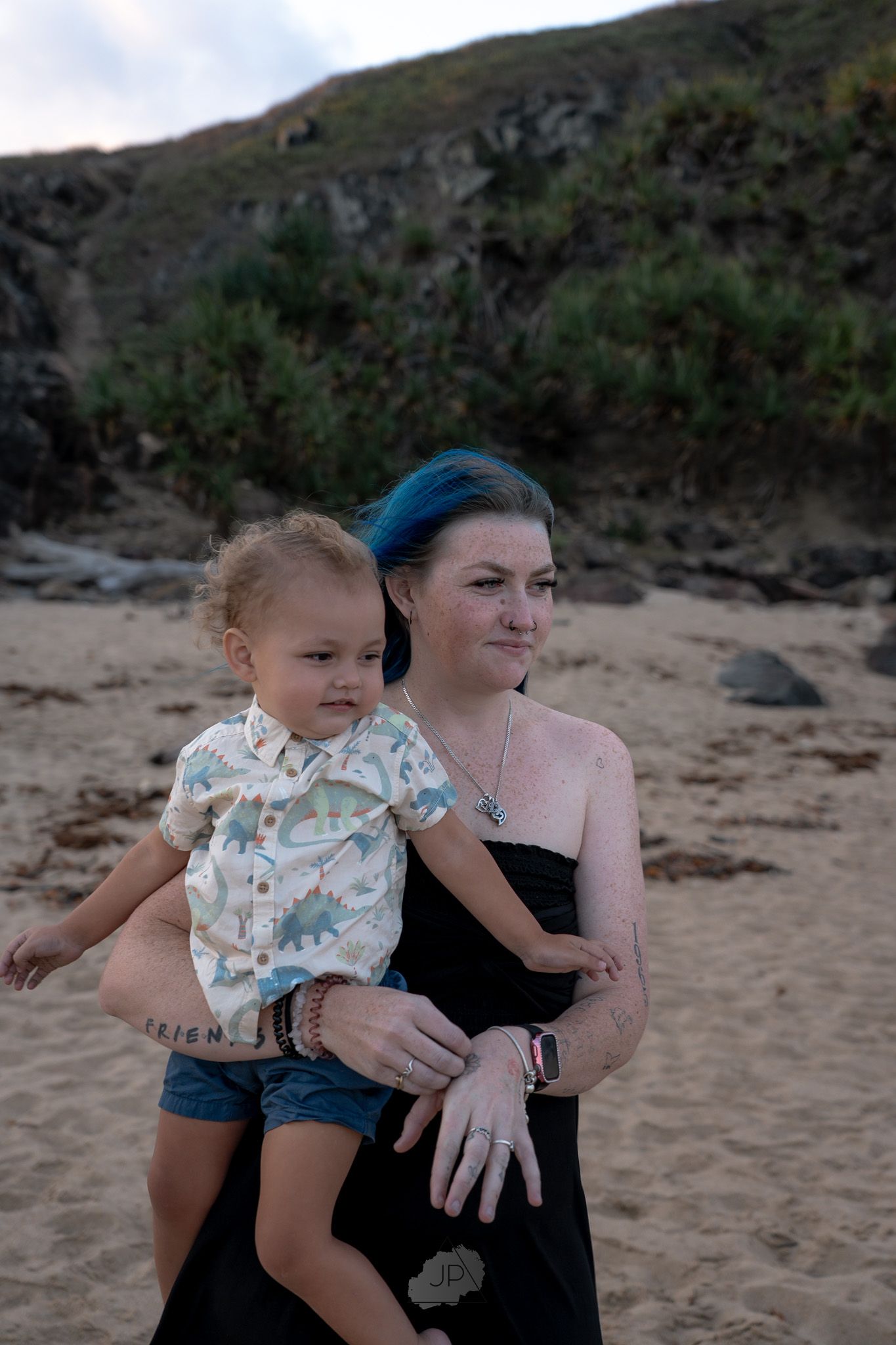 A mother and child share a tender moment together on a beach with rocky cliffs in the background.