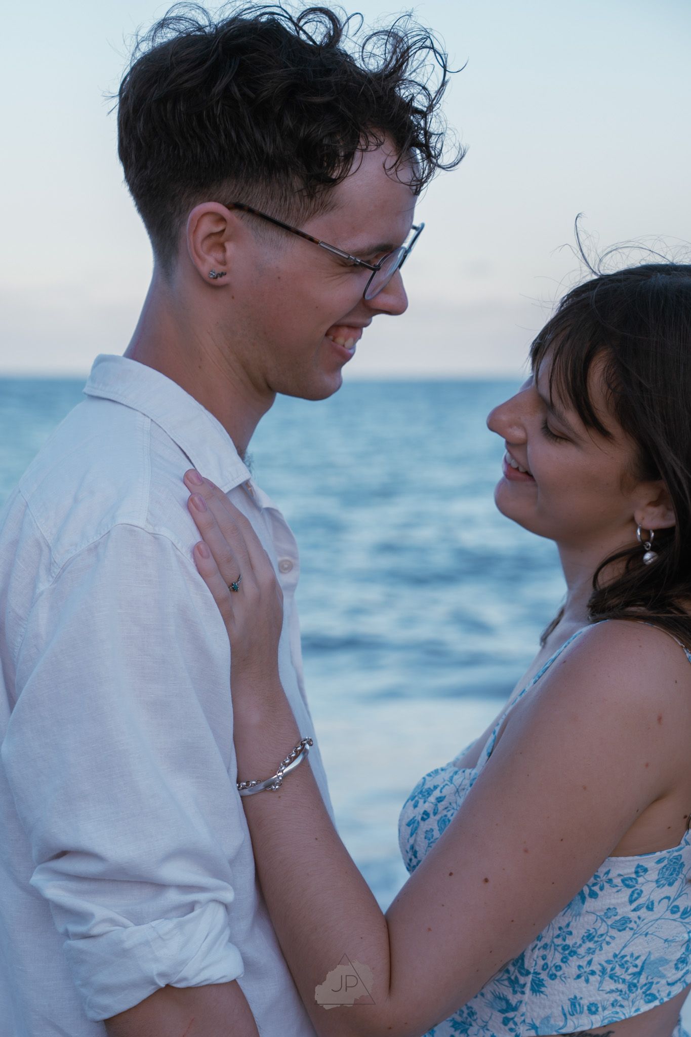 Romantic couple embraces on beach at sunset with ocean waves in background.