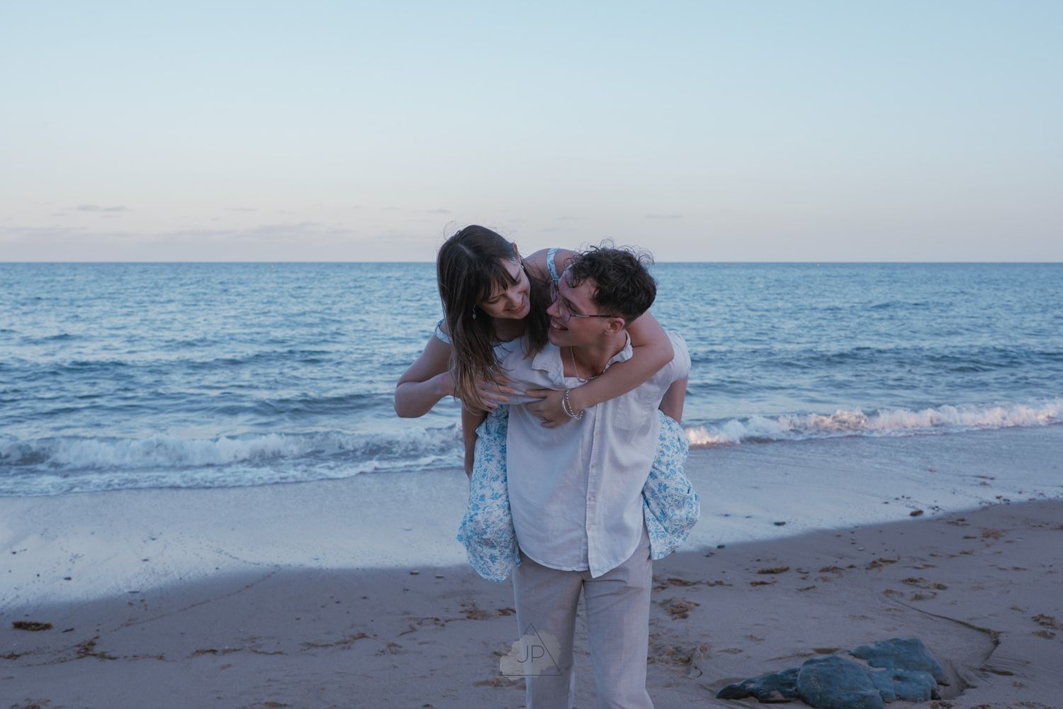 Romantic couple embracing on a beach at sunset with waves crashing in the background.