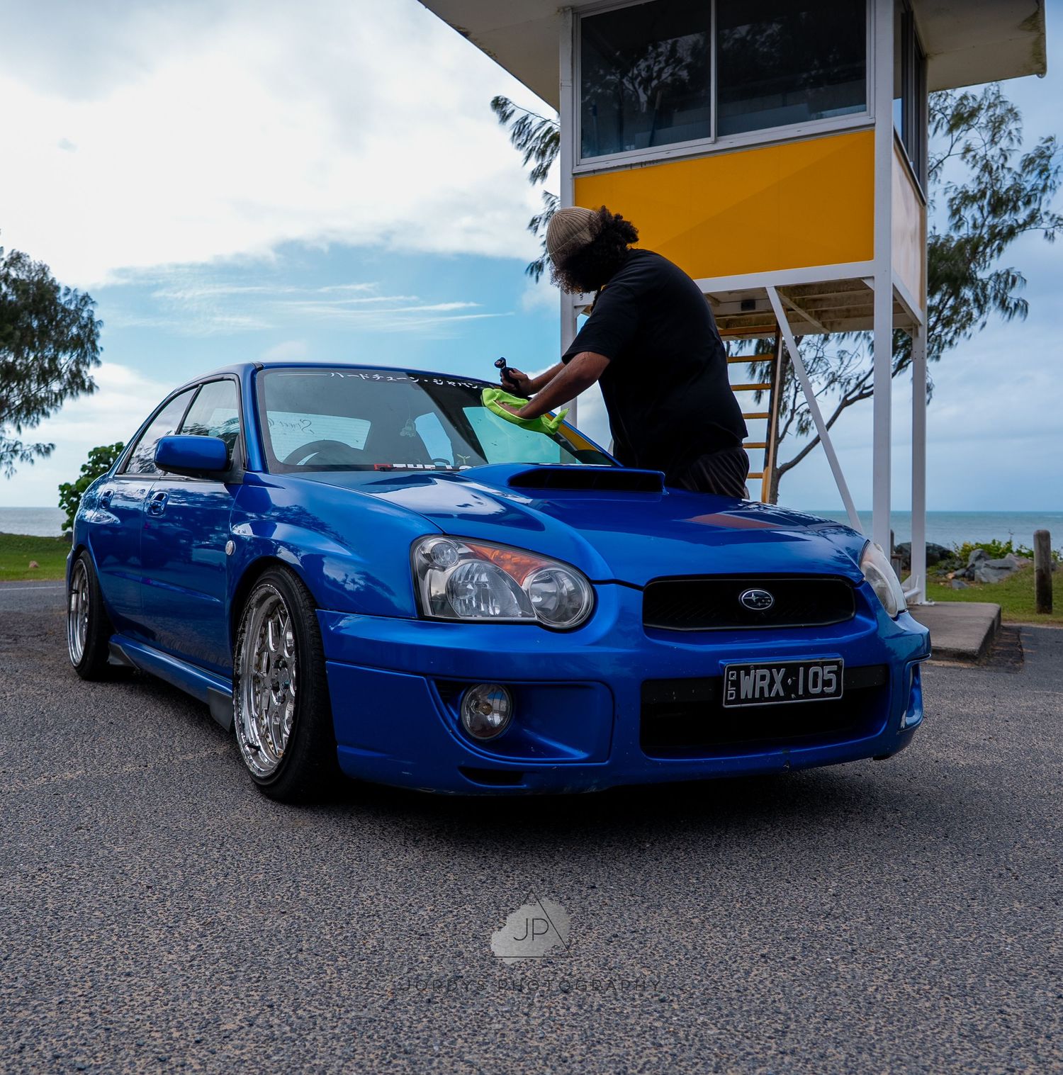 A bright blue Subaru WRX STI sports car with aftermarket wheels parked at a gas station during sunset.