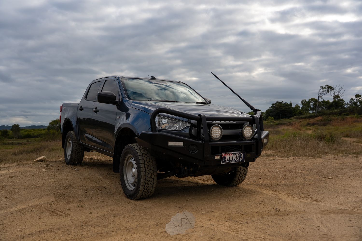 Lifted 4x4 pickup truck with bull bar and off-road modifications parked on dirt under cloudy skies.