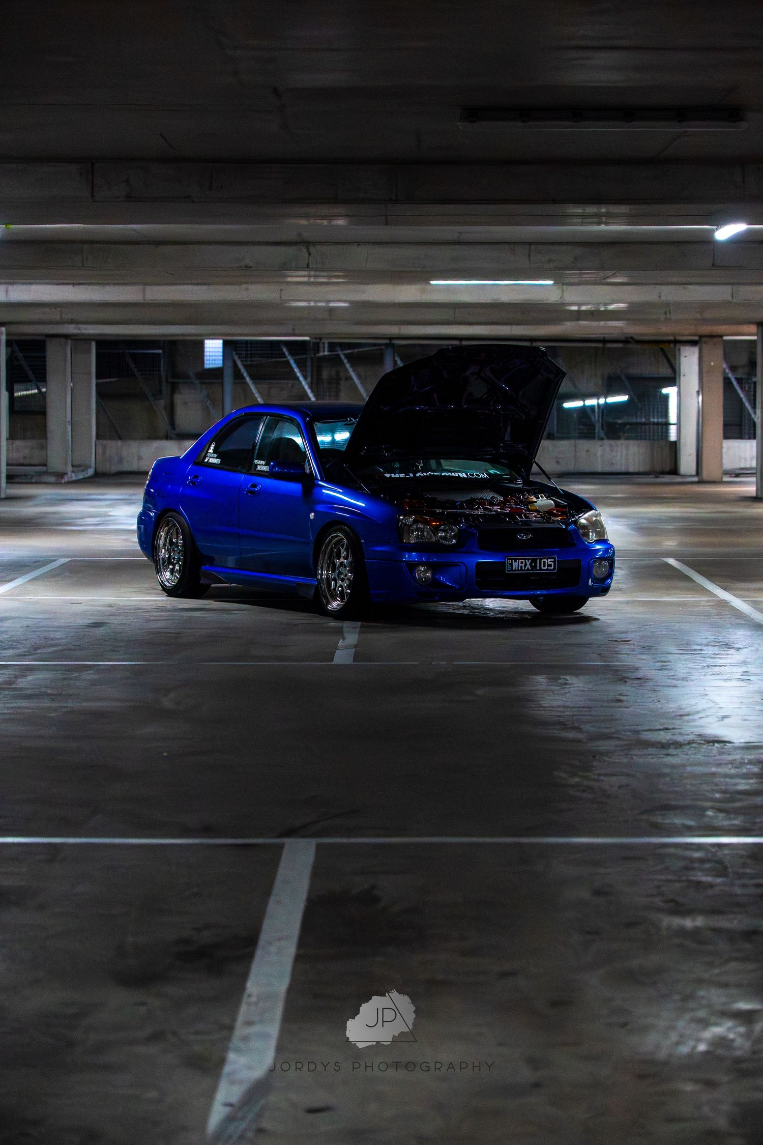 Blue modified Nissan 240SX sports car parked in dimly lit underground parking garage with atmospheric lighting.