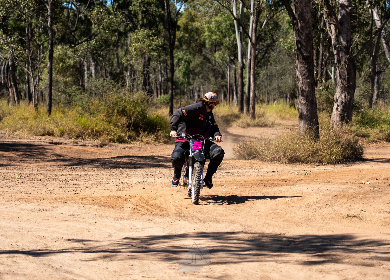 A sequence of people walking along a dirt trail through eucalyptus trees in an Australian bush setting.