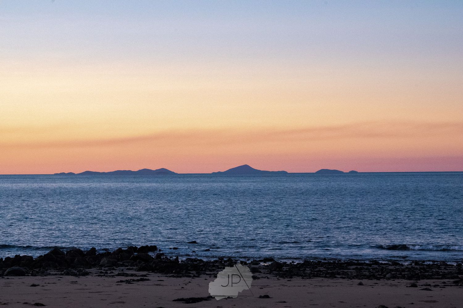 Beautiful blue and pink sunset sky blending over calm ocean waters with silhouetted mountains in the distance.