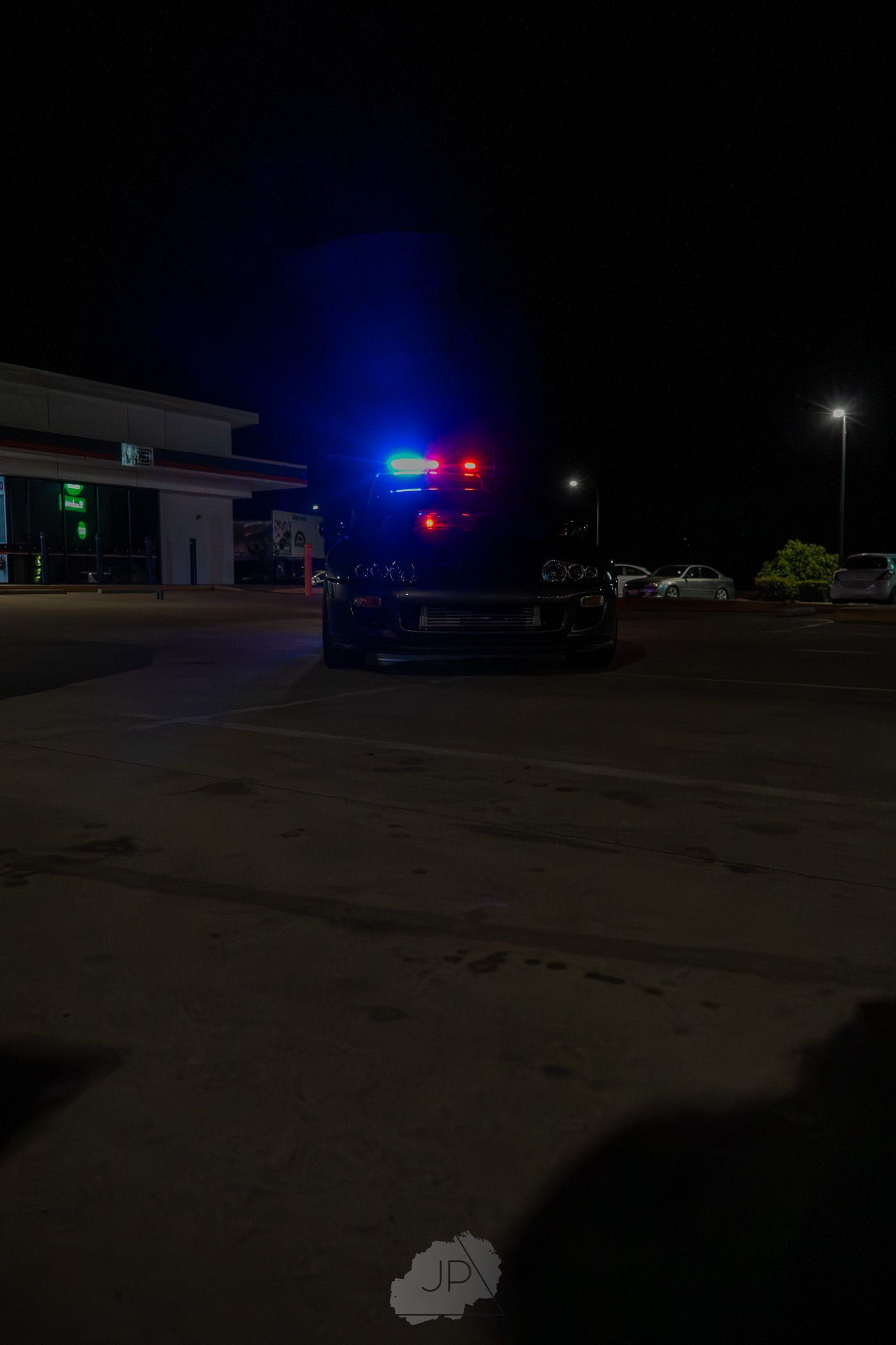 A police vehicle with flashing red and blue lights illuminates a dark parking lot at night.