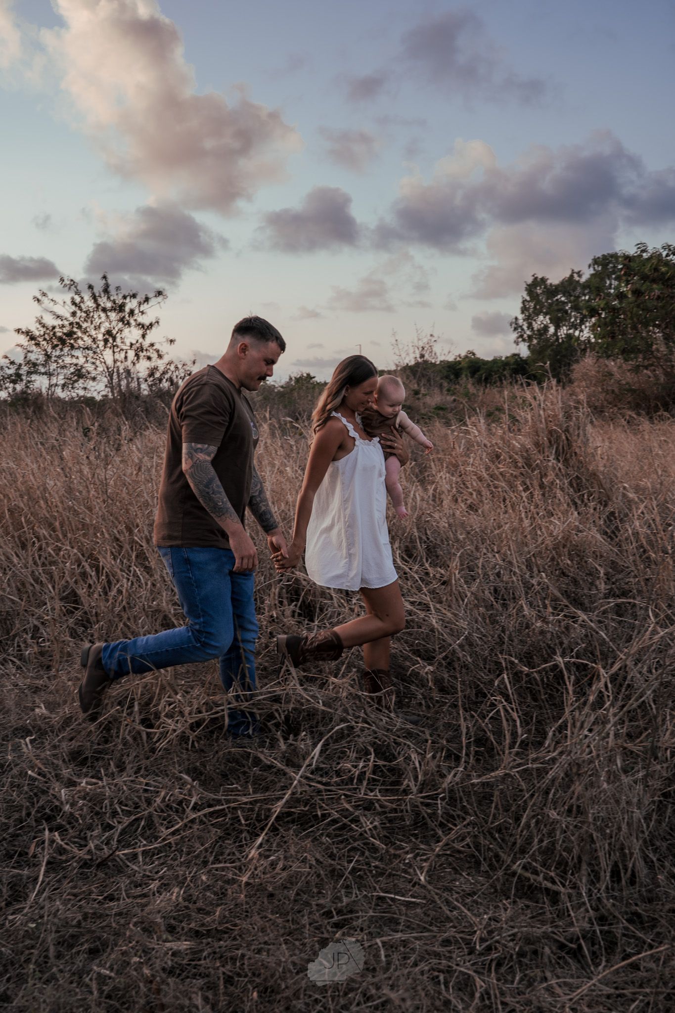 A couple shares a romantic moment at sunset in a field of dried brush and grass.