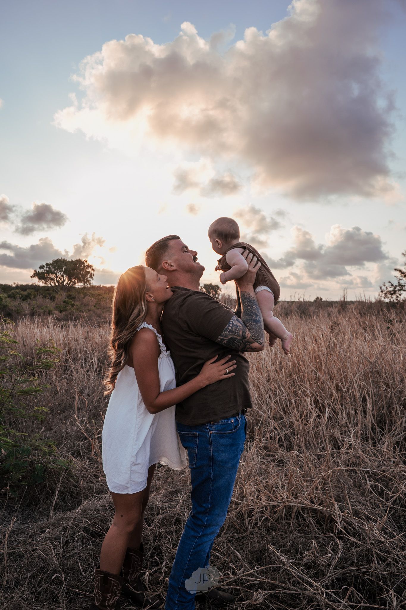 A couple shares tender moments in a field of tall grass during sunset.