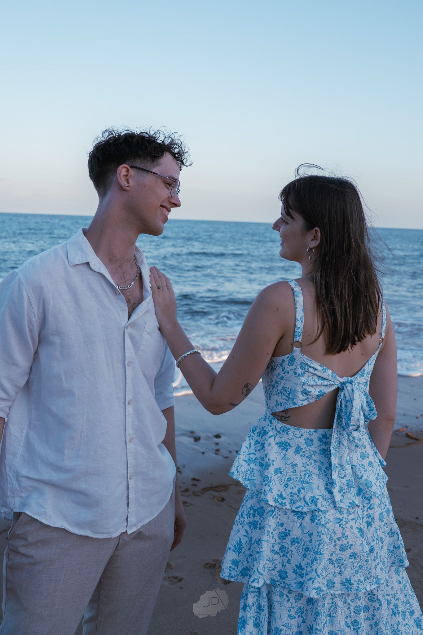 A couple in beachwear shares playful moments along the shoreline at sunset.