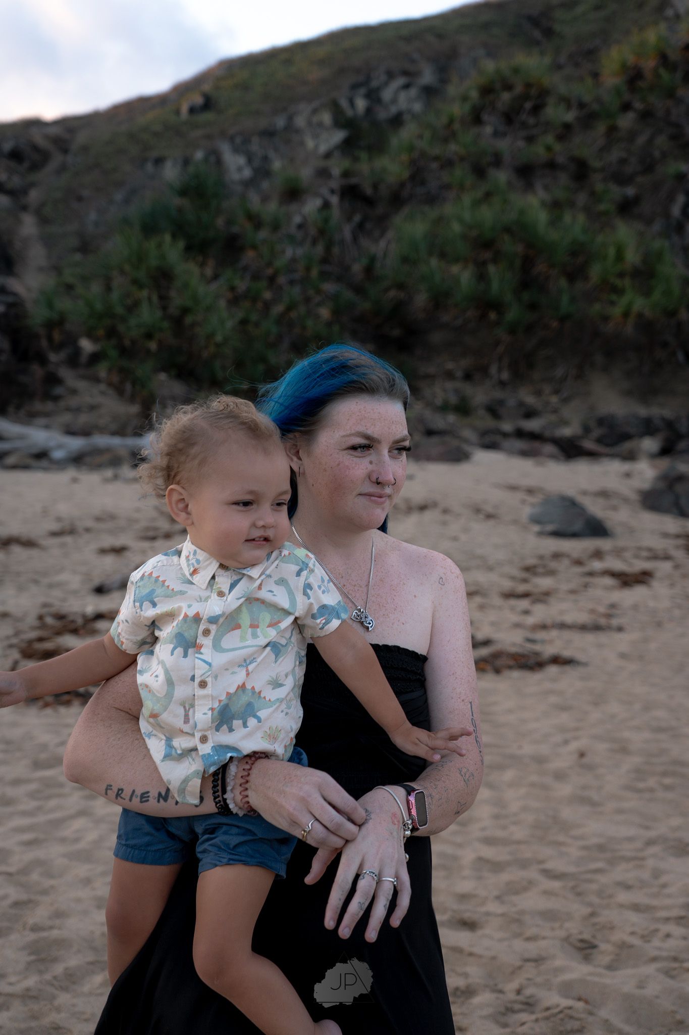 A parent and toddler share a tender moment together on a sandy beach with mountains in the background.