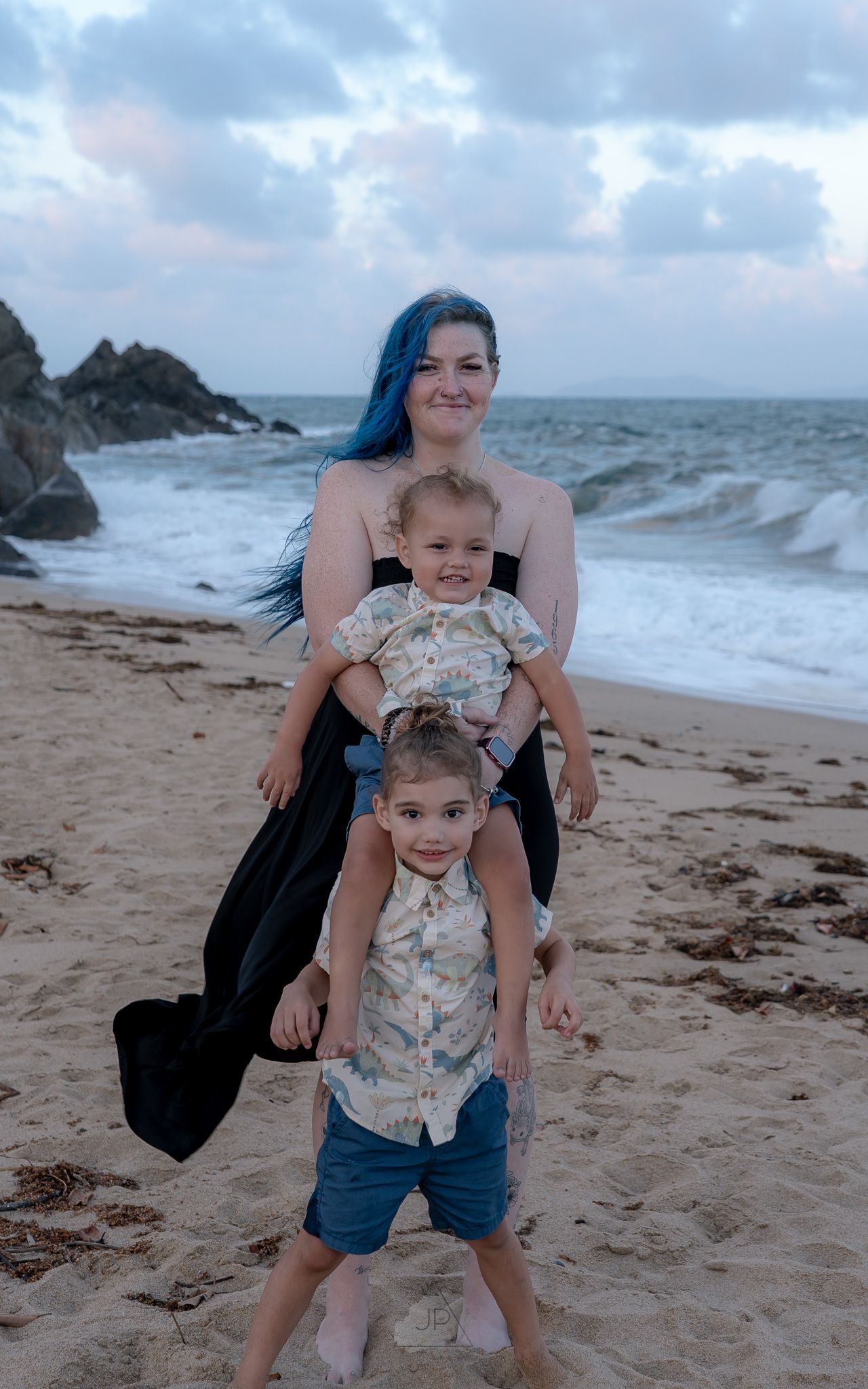 A family poses together on a beach with rocky cliffs and stormy waves in the background at sunset.