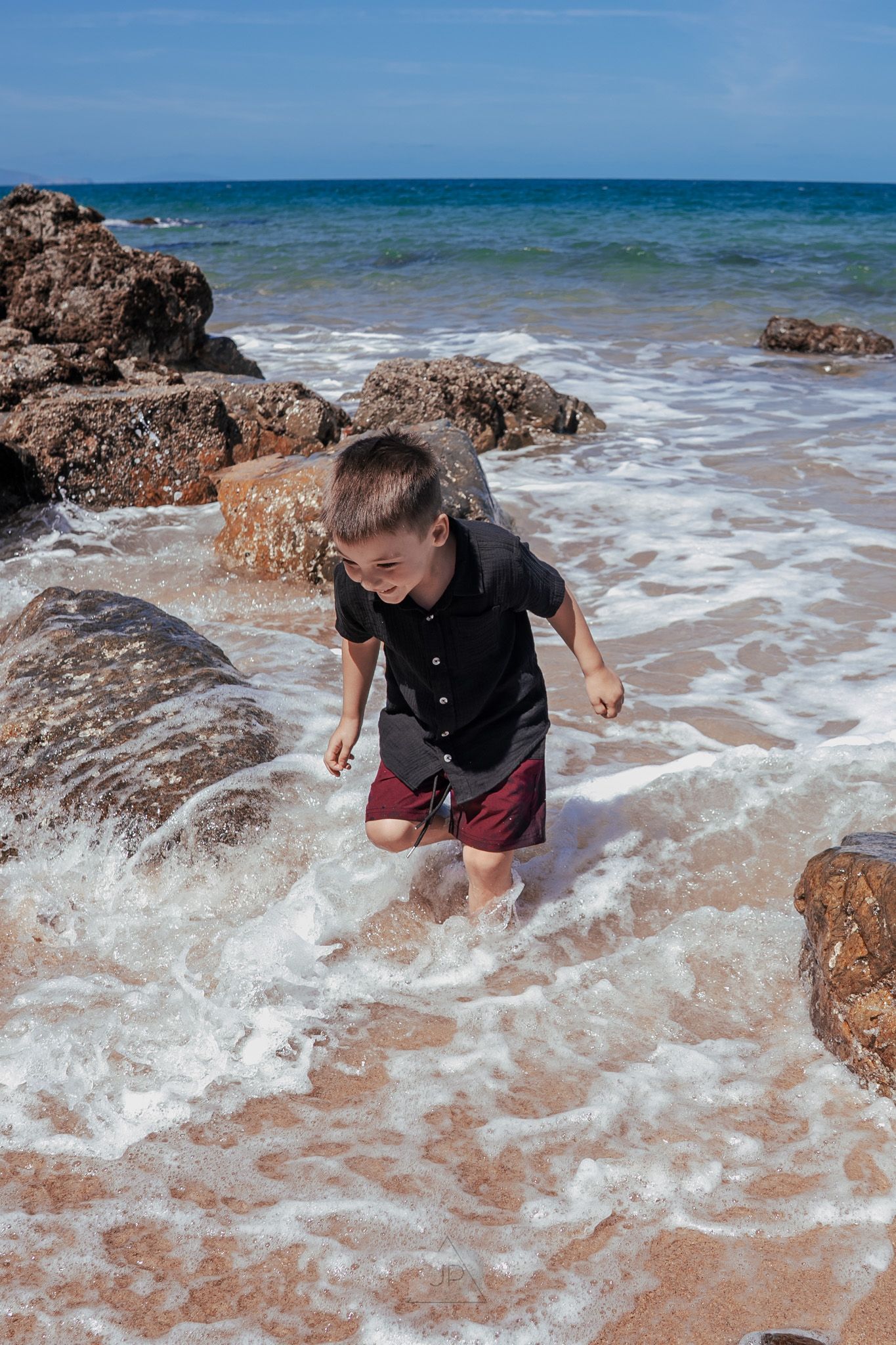 Ocean waves splash around coastal rocks as someone explores the shoreline during low tide.