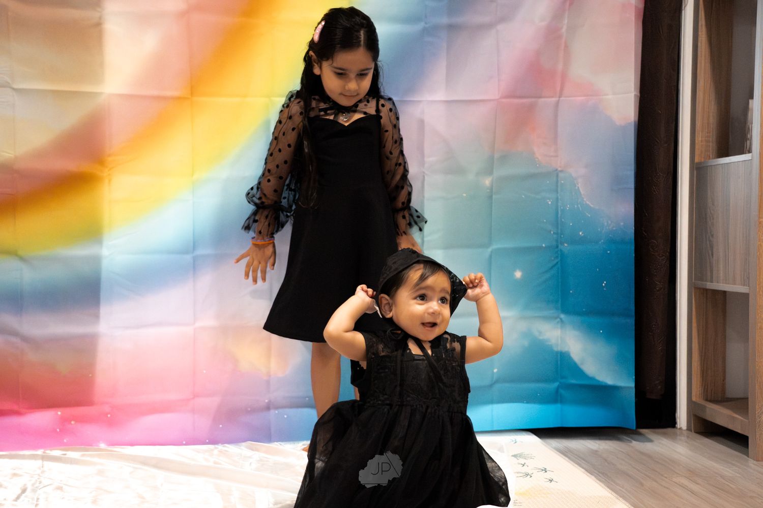 A young child in a black outfit plays and moves energetically in a hallway with colorful wall decorations.