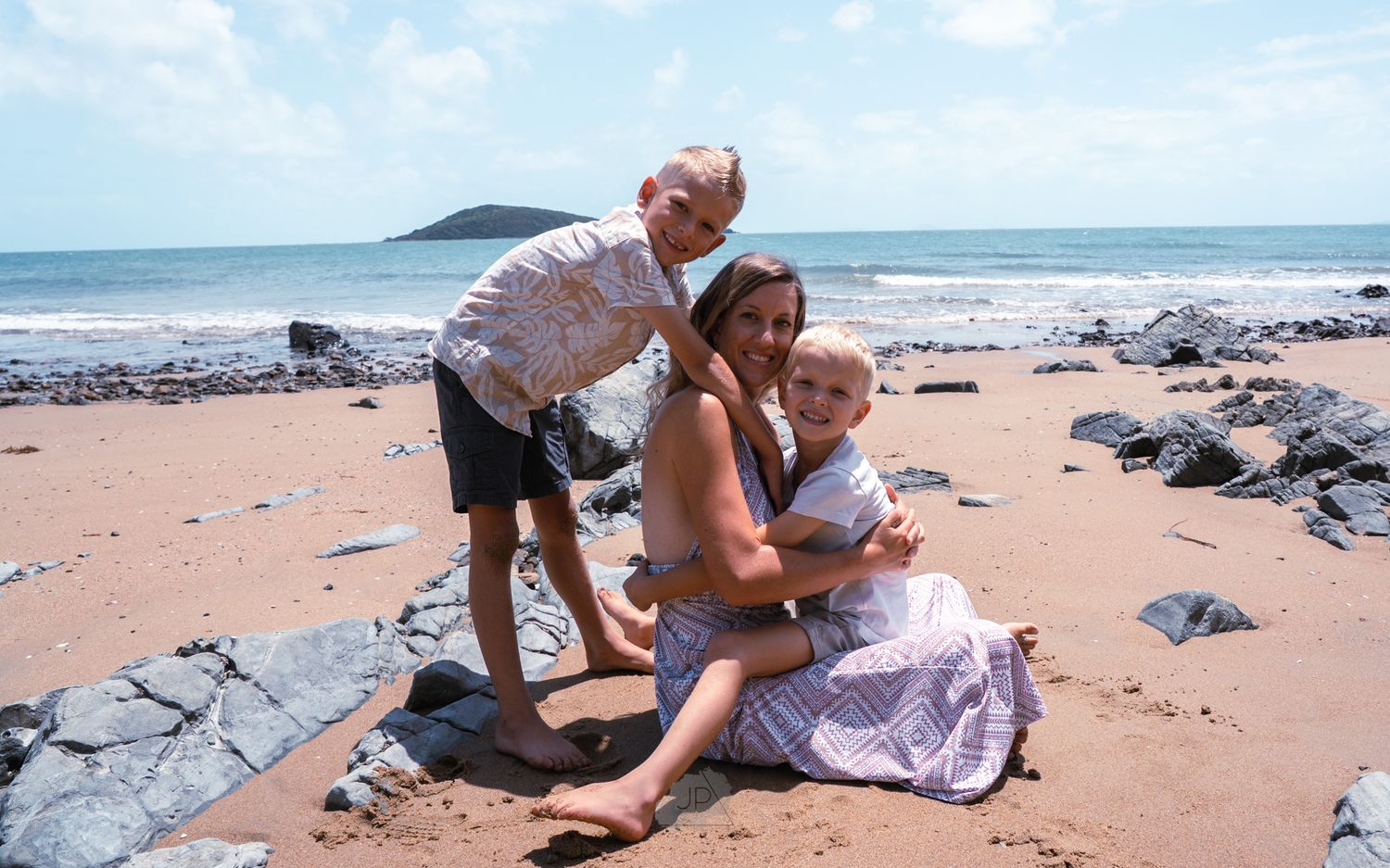 People enjoying a sunny day at a rocky beach with ocean waves and blue sky in the background.