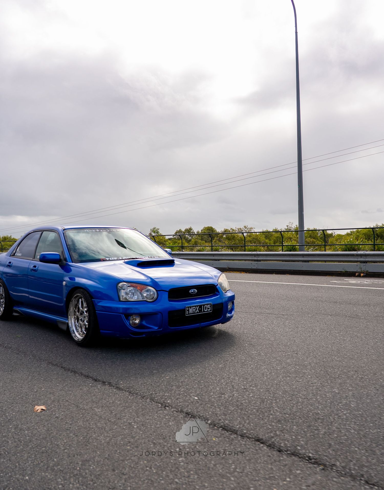 A bright blue Subaru WRX STI with custom wheels shown from different angles along a coastal roadway.