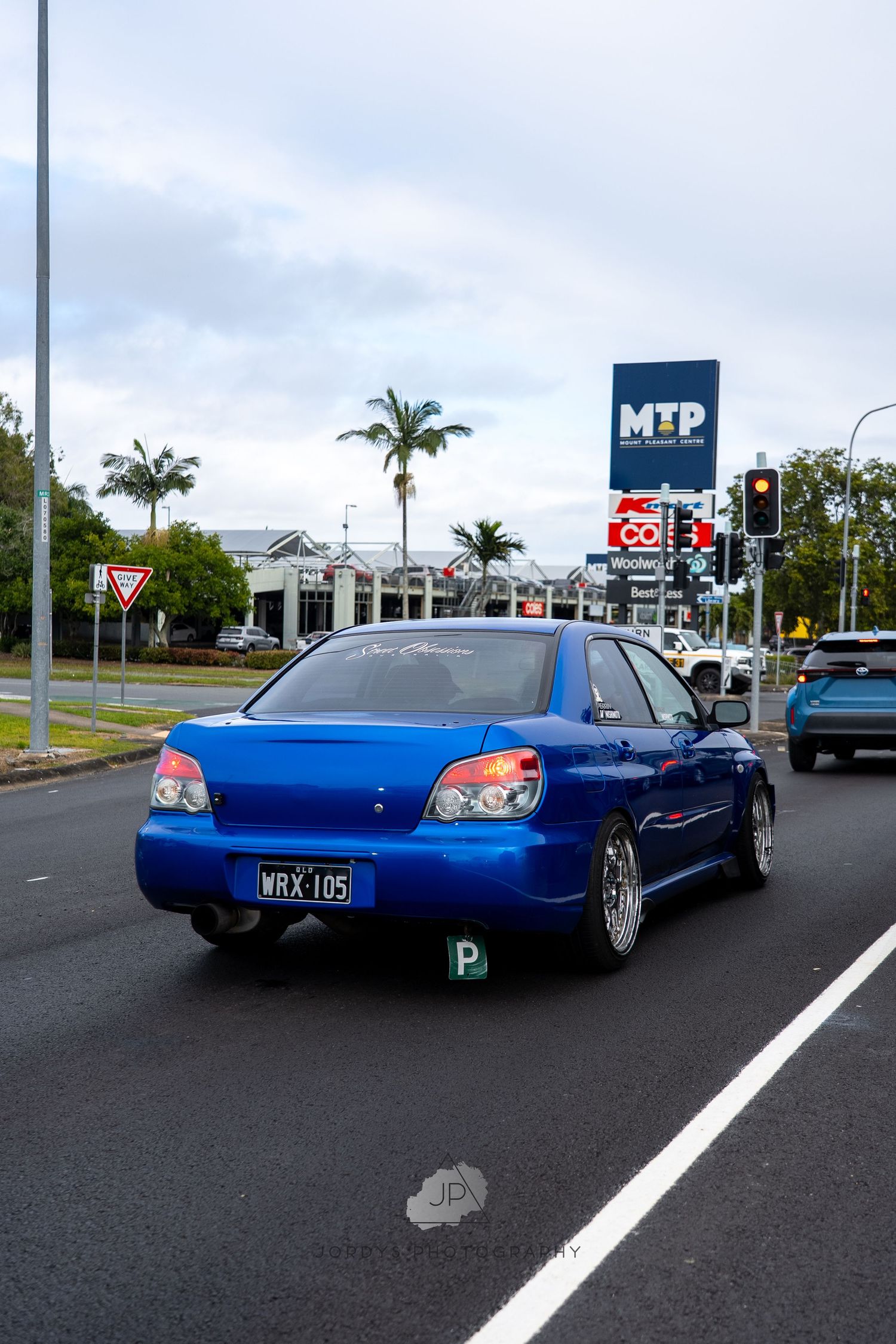 A lowered blue Subaru Impreza sedan with custom modifications parked in a parking lot at dusk.