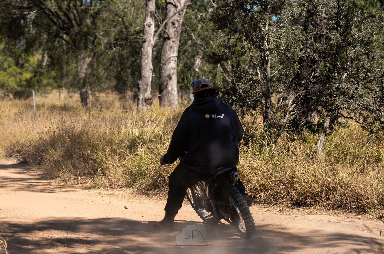 A cyclist in dark clothing rides along a dirt trail through trees and dried grass during daytime.
