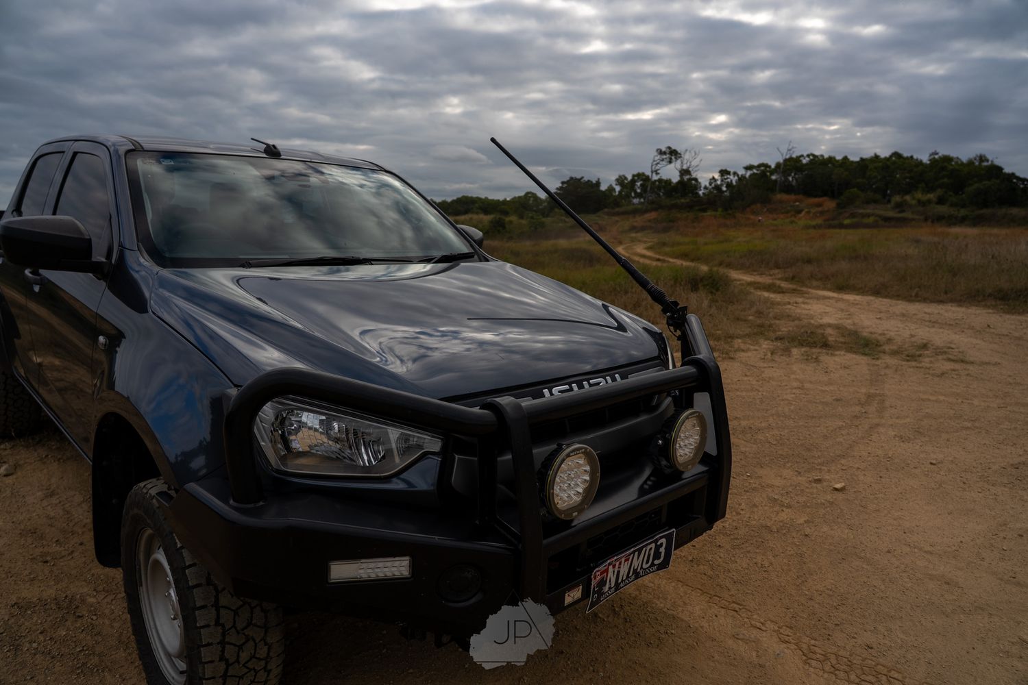 A set of black BMW vehicles parked on a dirt road under dramatic cloudy skies.