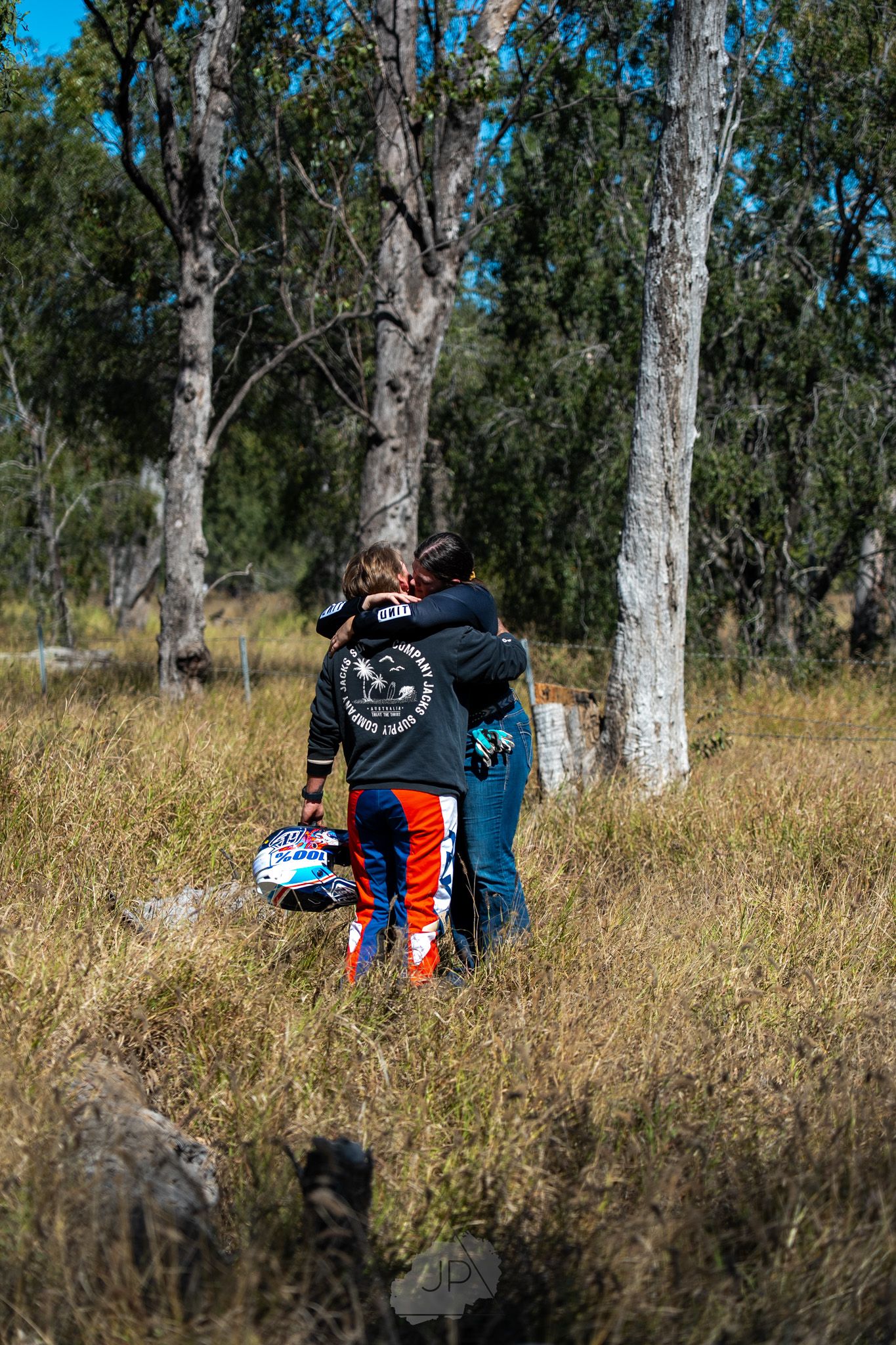 A person is sitting on a grassy hillside among eucalyptus trees with a backpack on a sunny day.