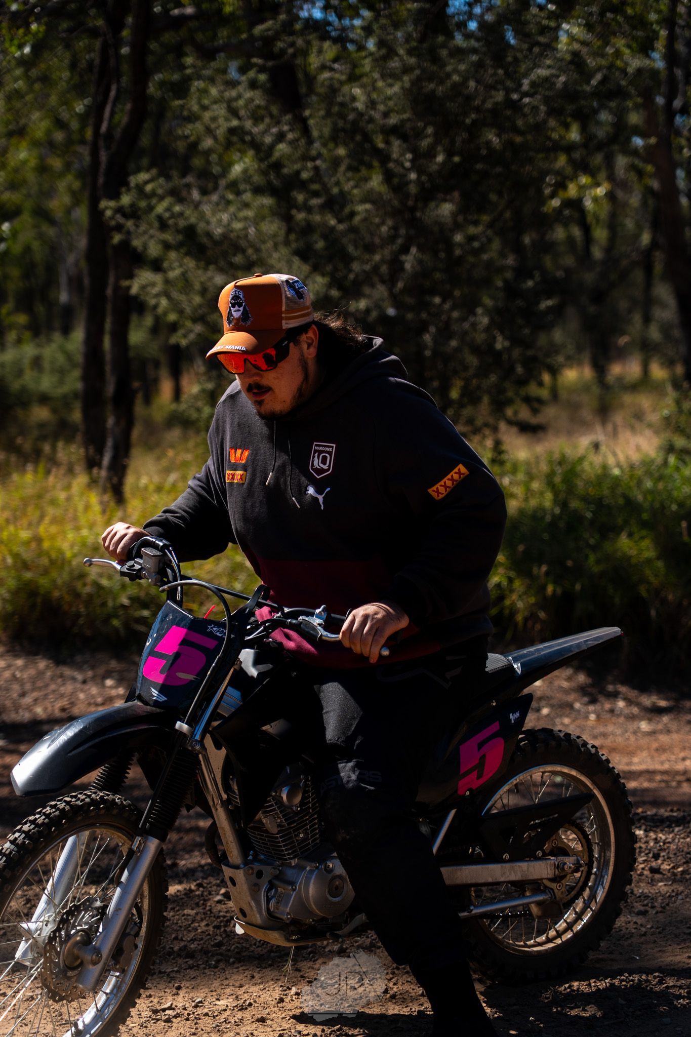 Multiple action shots of a dirt bike rider performing maintenance on a motorcycle in a wooded setting.