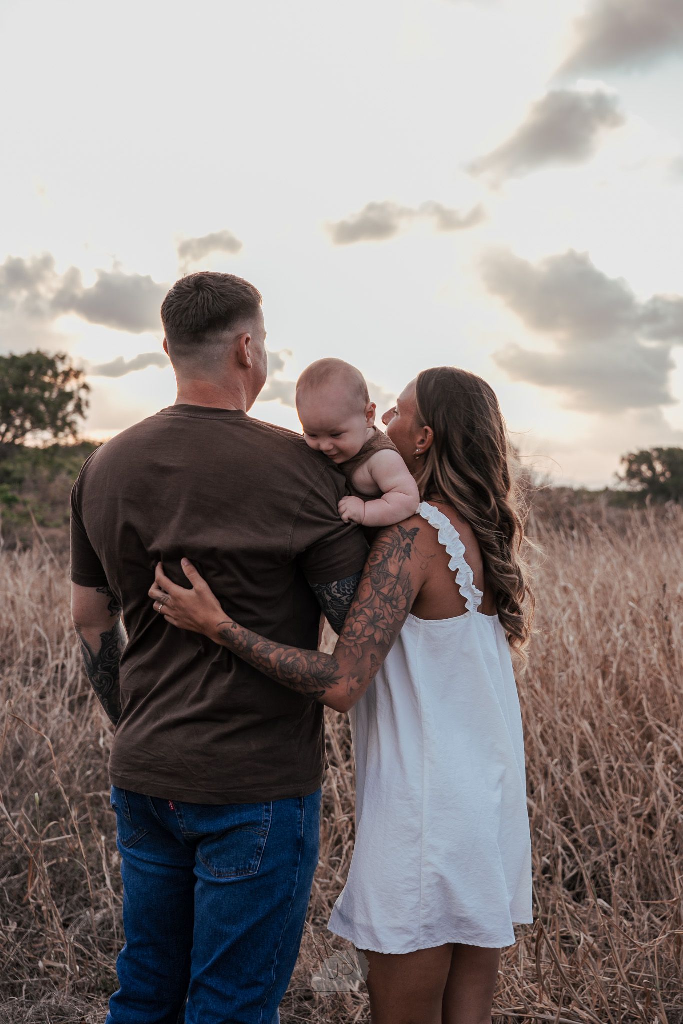 A touching family moment captured in a field at sunset with warm embraces and laughter.