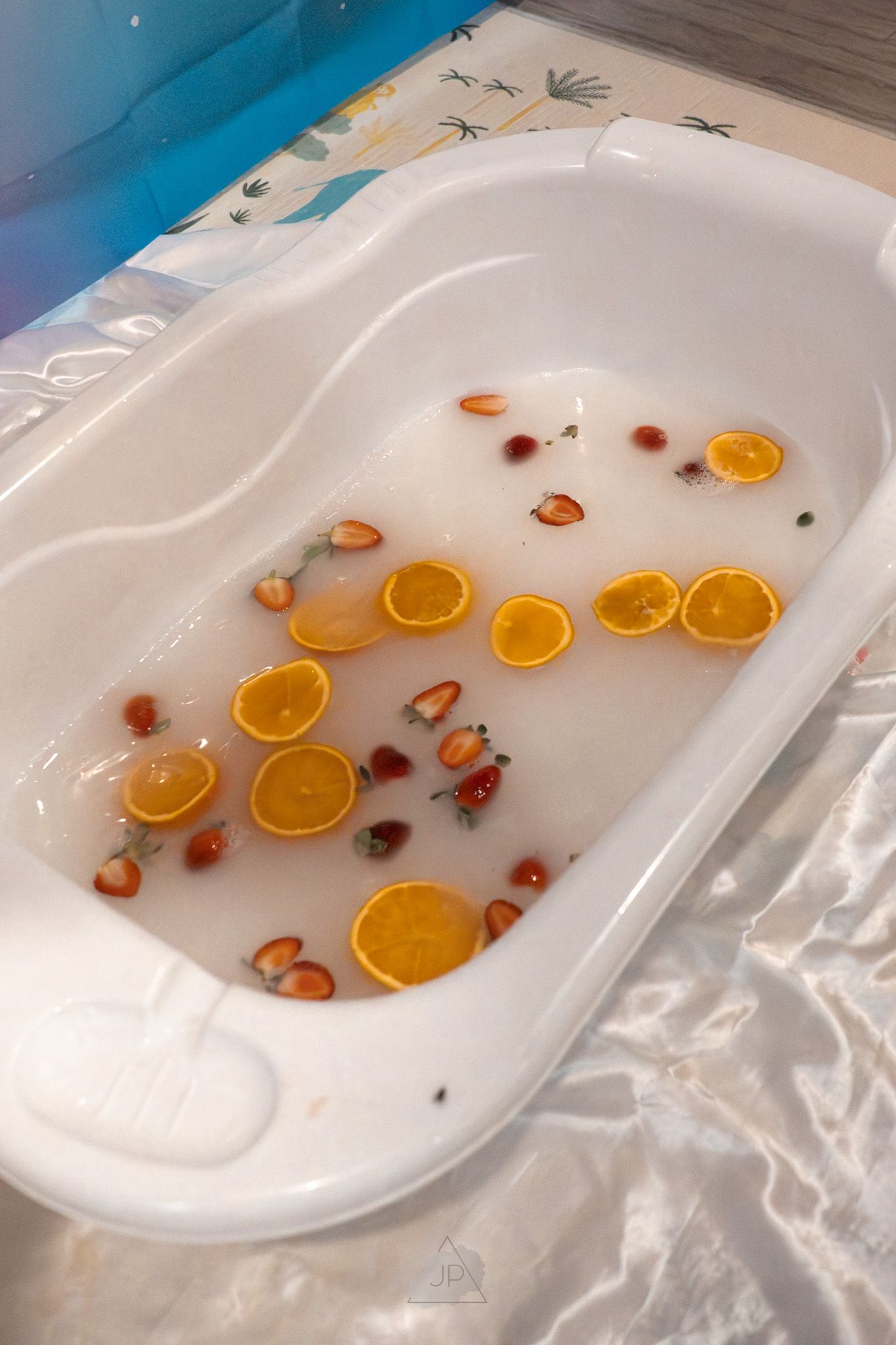 A white bathtub filled with floating orange slices and rose petals creates a luxurious spa-like setting.