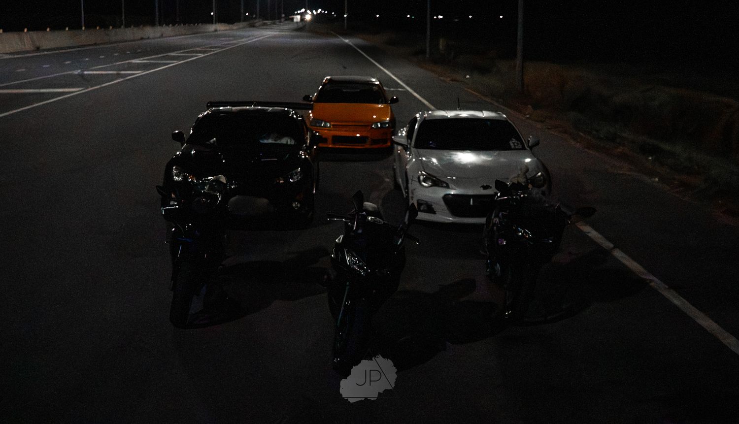 Multiple dark vehicles driving on a highway at night with illuminated headlights and taillights visible.
