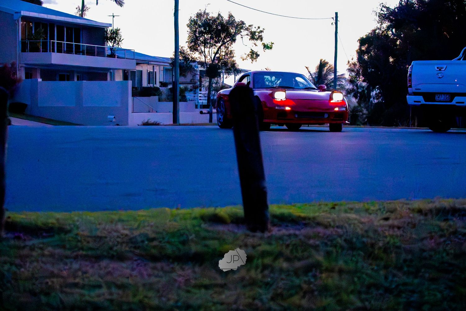 Long exposure photo captures blue hour at dusk with car light trails streaking through a suburban street scene.
