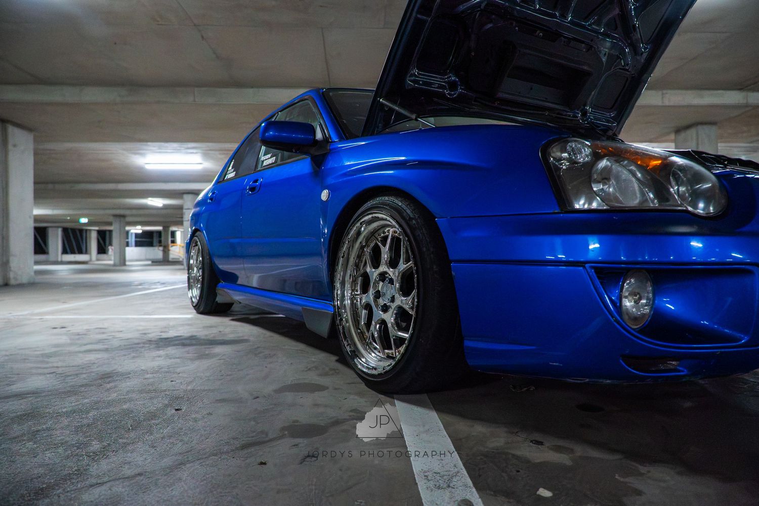 Multiple side profile views of a bright blue Ferrari F40 supercar parked in a dimly lit garage space.