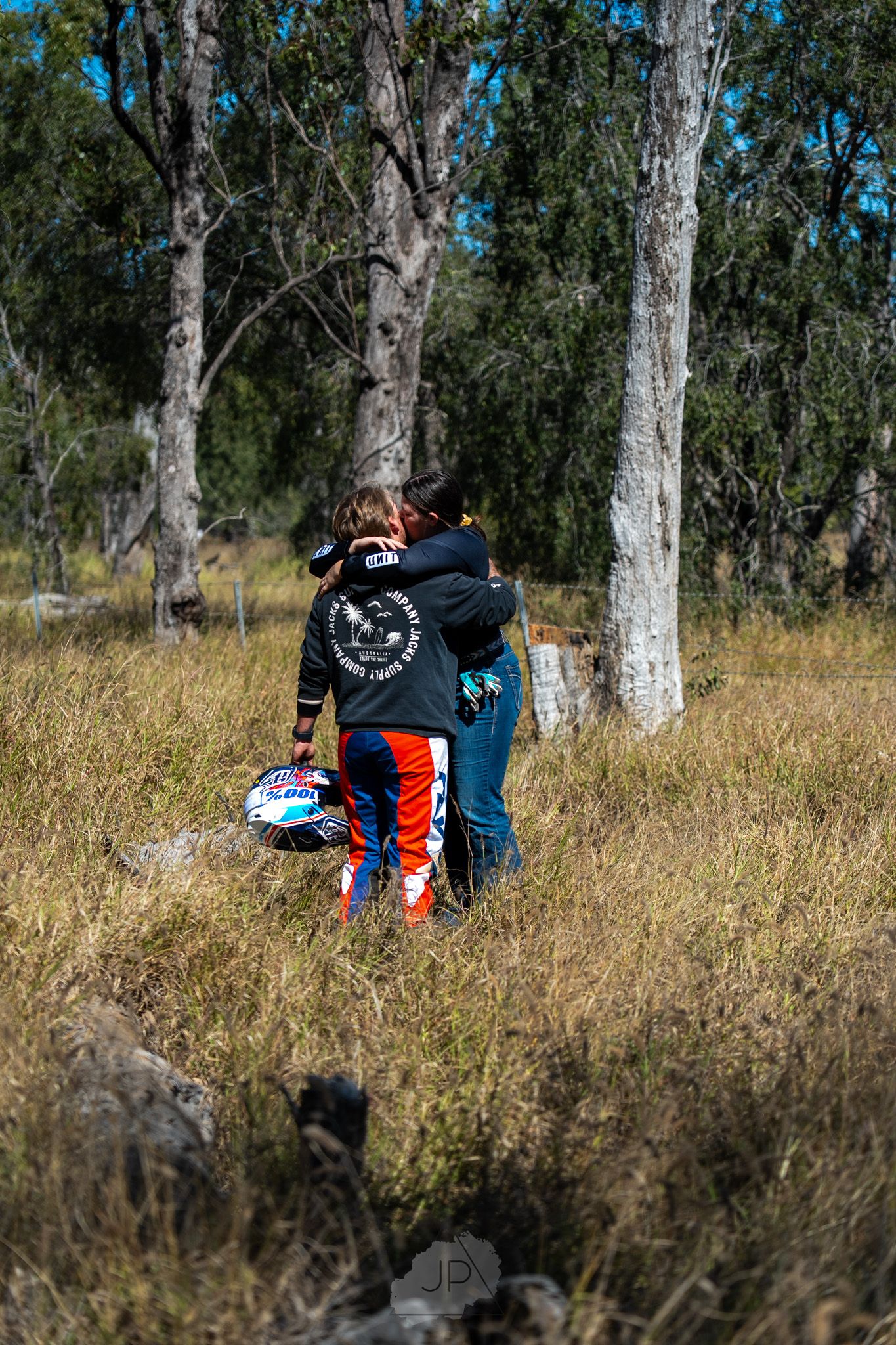 Person resting on grassy hill among tall eucalyptus trees with backpack and camping gear.