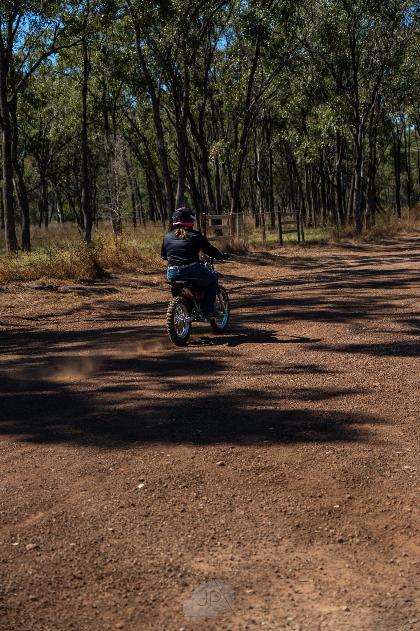 Motorcyclist riding on a dirt path through an Australian bush landscape with tall eucalyptus trees.
