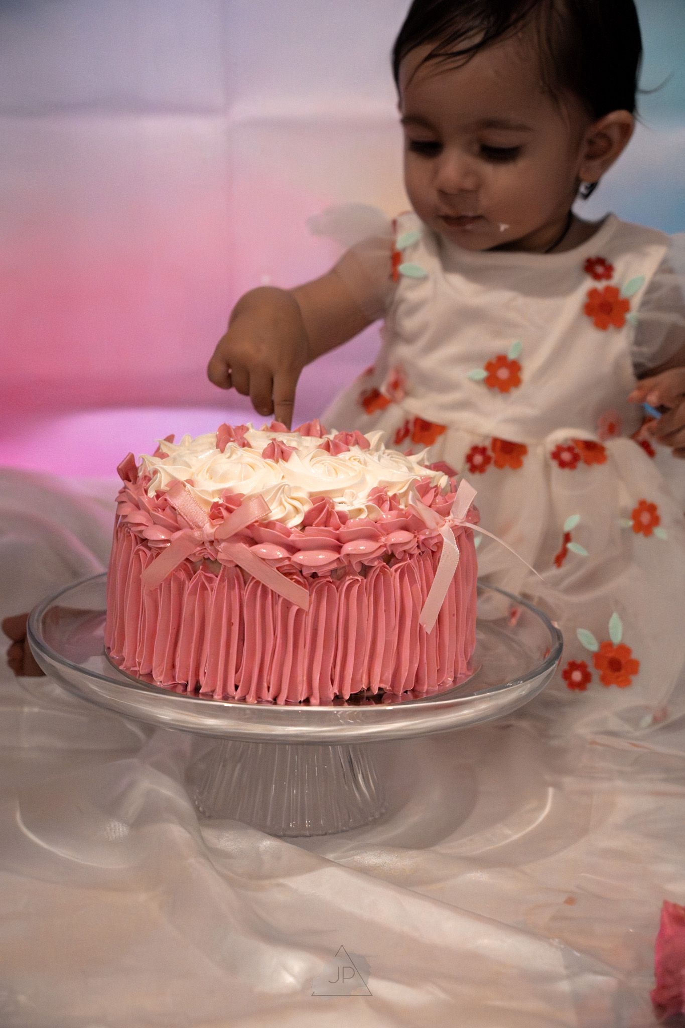 Pink frosted birthday cake with peppermint candies on glass cake stand being served at a festive celebration.