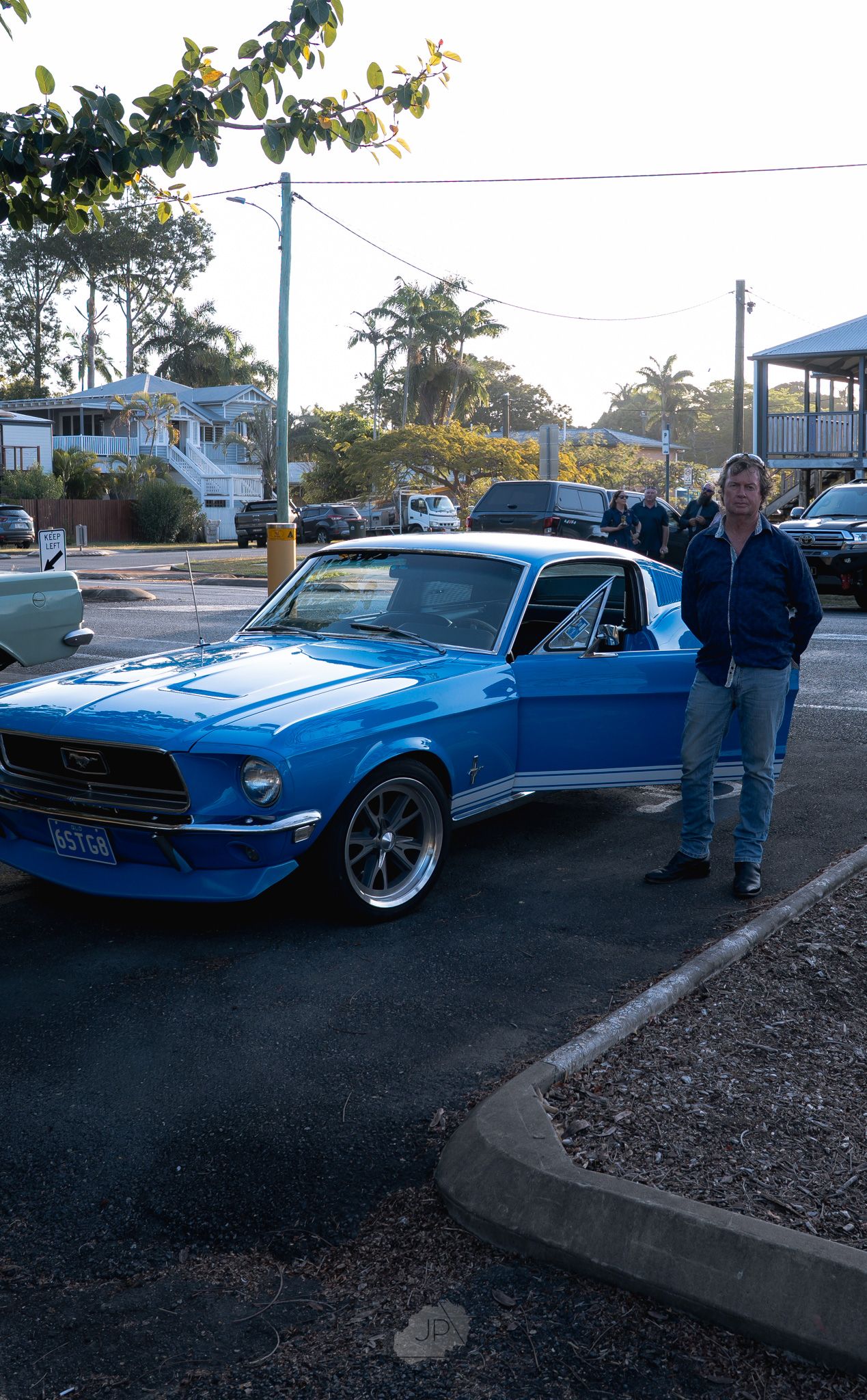 A classic blue Ford Mustang convertible with custom wheels parked on a street at dusk.
