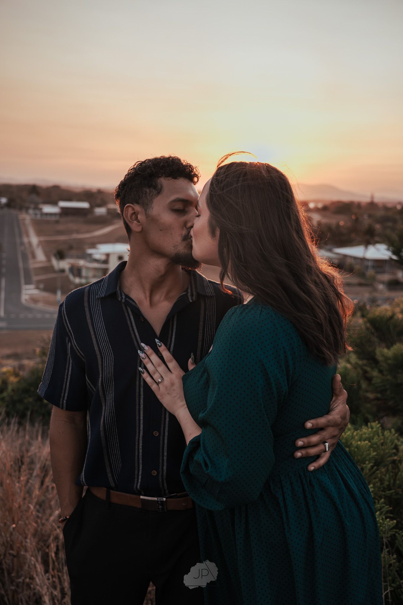 A romantic couple embraces against a sunset cityscape backdrop during an intimate photoshoot.