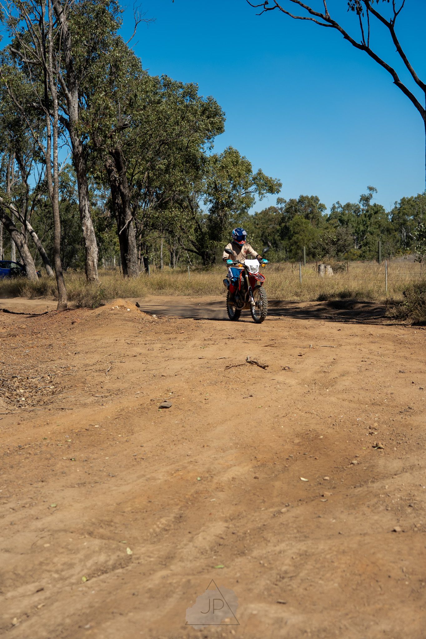 An off-road dirt path curves through Australian bushland with scattered eucalyptus trees along the trail.