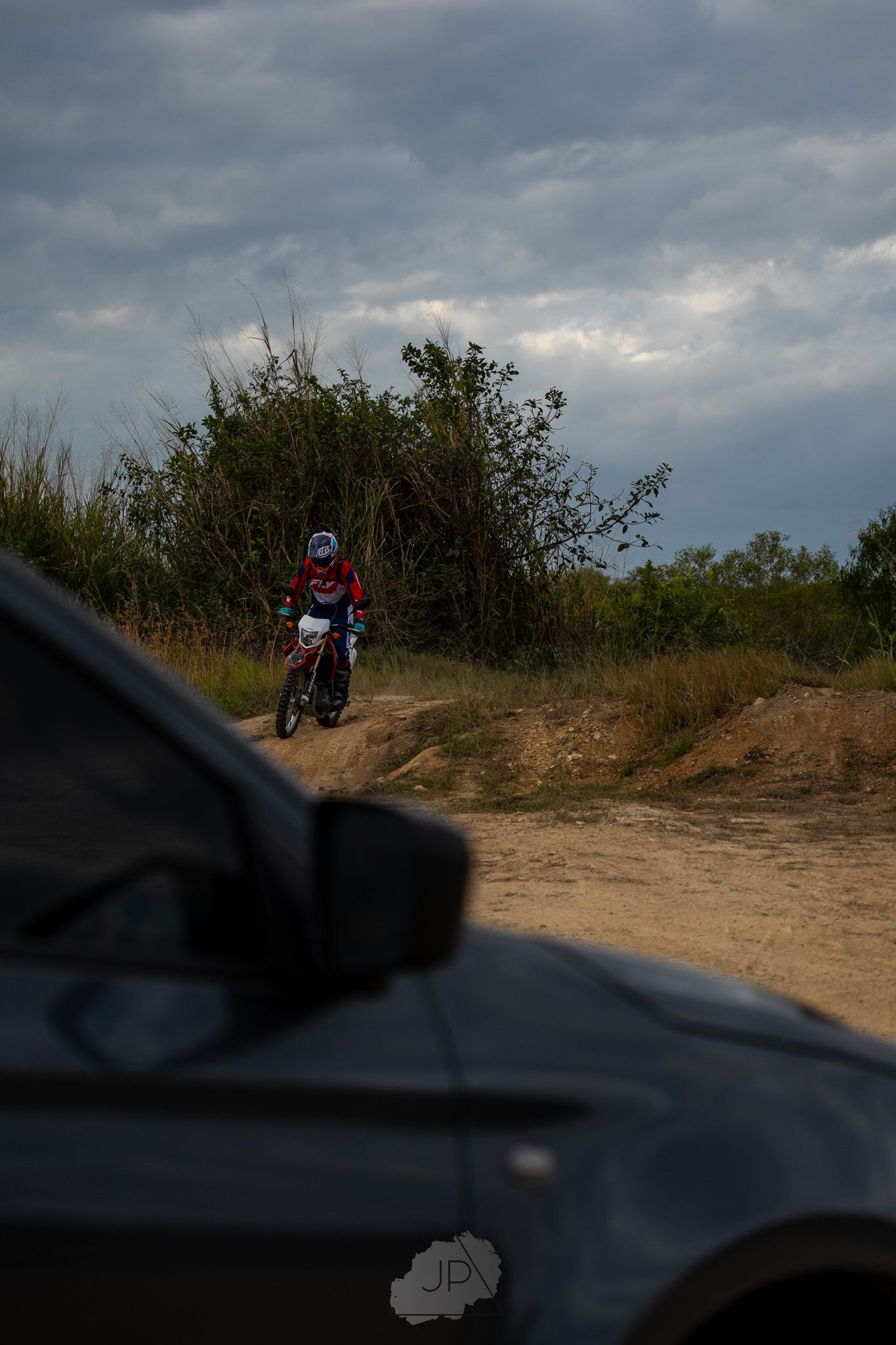 Red and white motorcycle riding along a scenic dirt trail beneath dramatic cloudy skies at dusk.