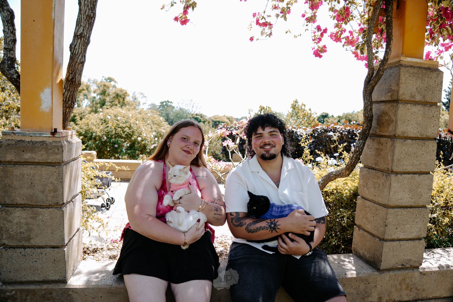 A couple sits together on stone steps in a romantic outdoor setting with flowering trees in the background.