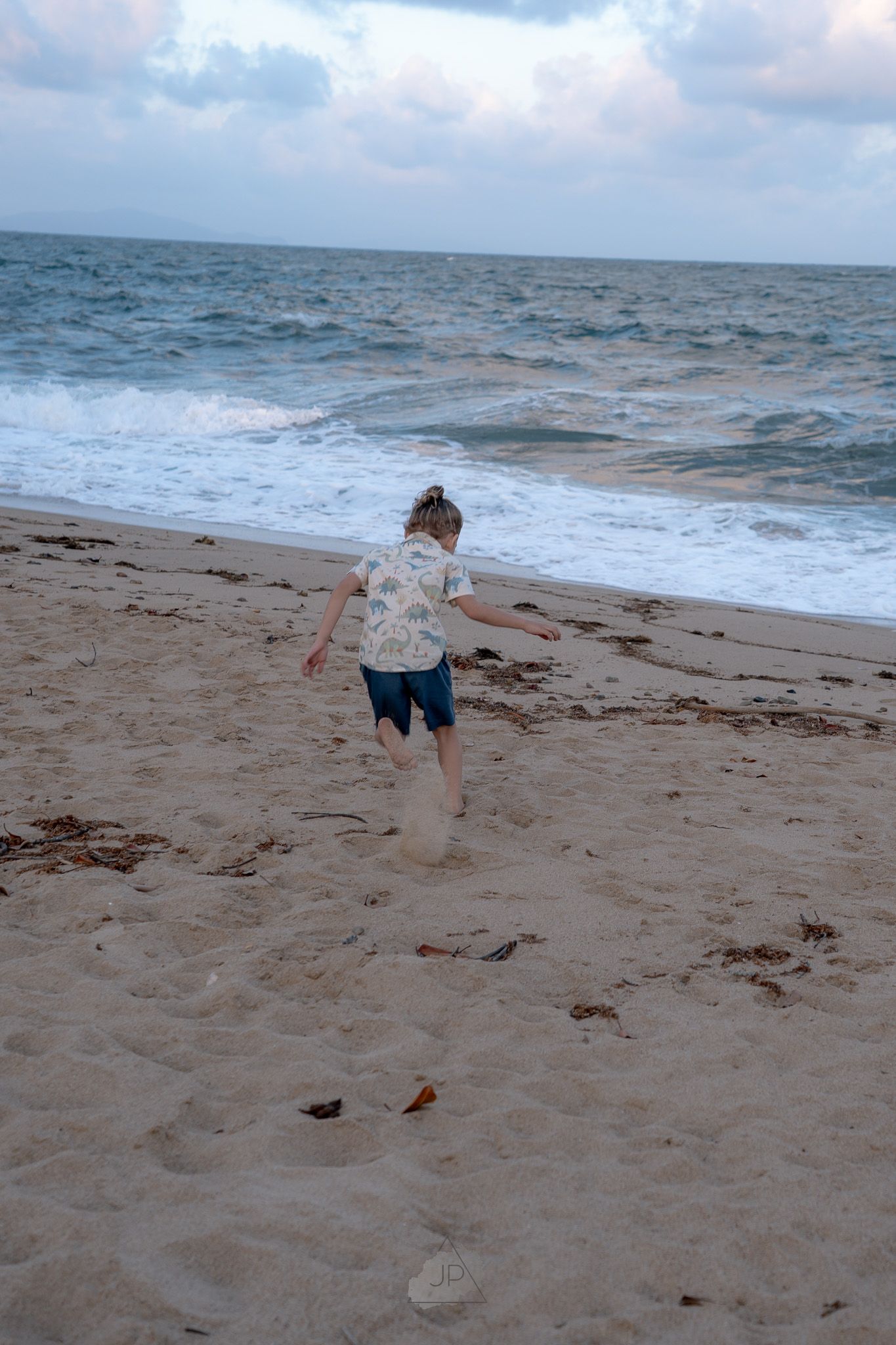 A child runs and plays along a sandy beach with ocean waves in the background.