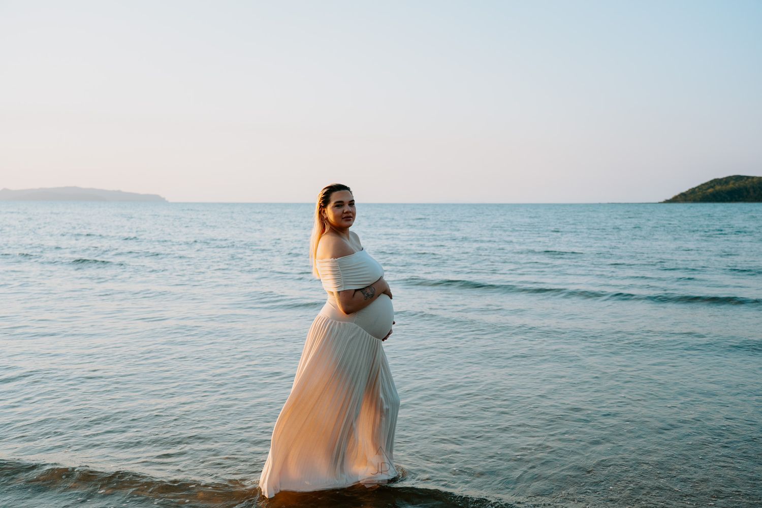 A scenic coastal landscape with calm ocean waters and distant hills under a soft blue sky.