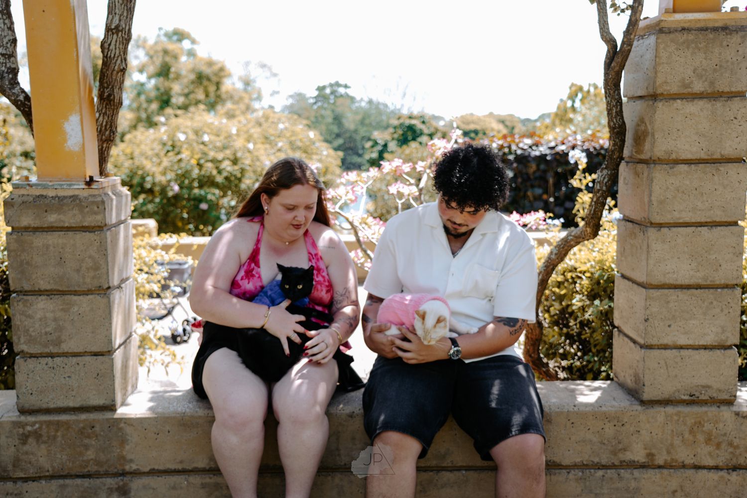 People sit and laugh together on stone steps in a sunny outdoor garden setting.