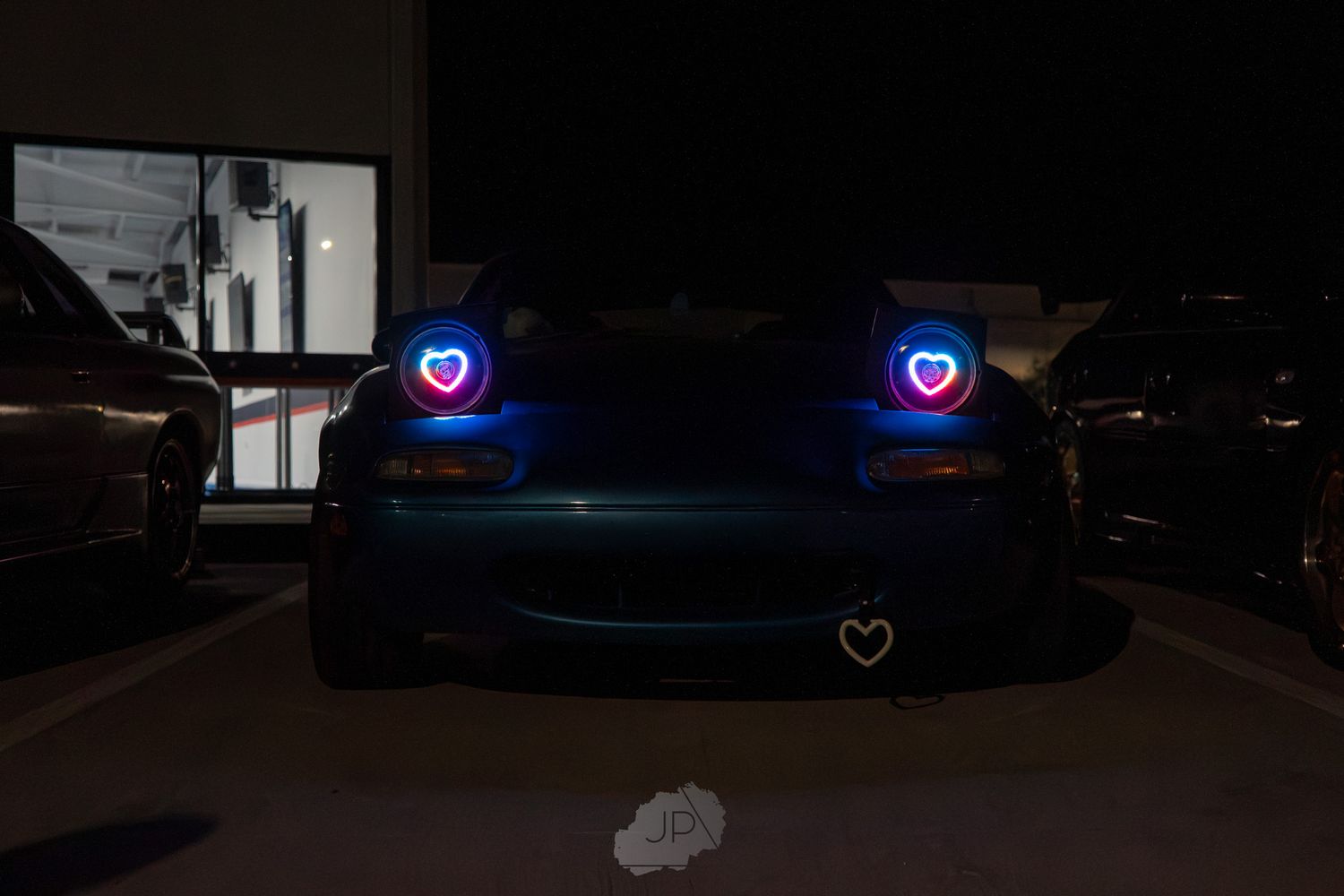 A series of modified cars with glowing blue LED lights parked in a dark parking garage.